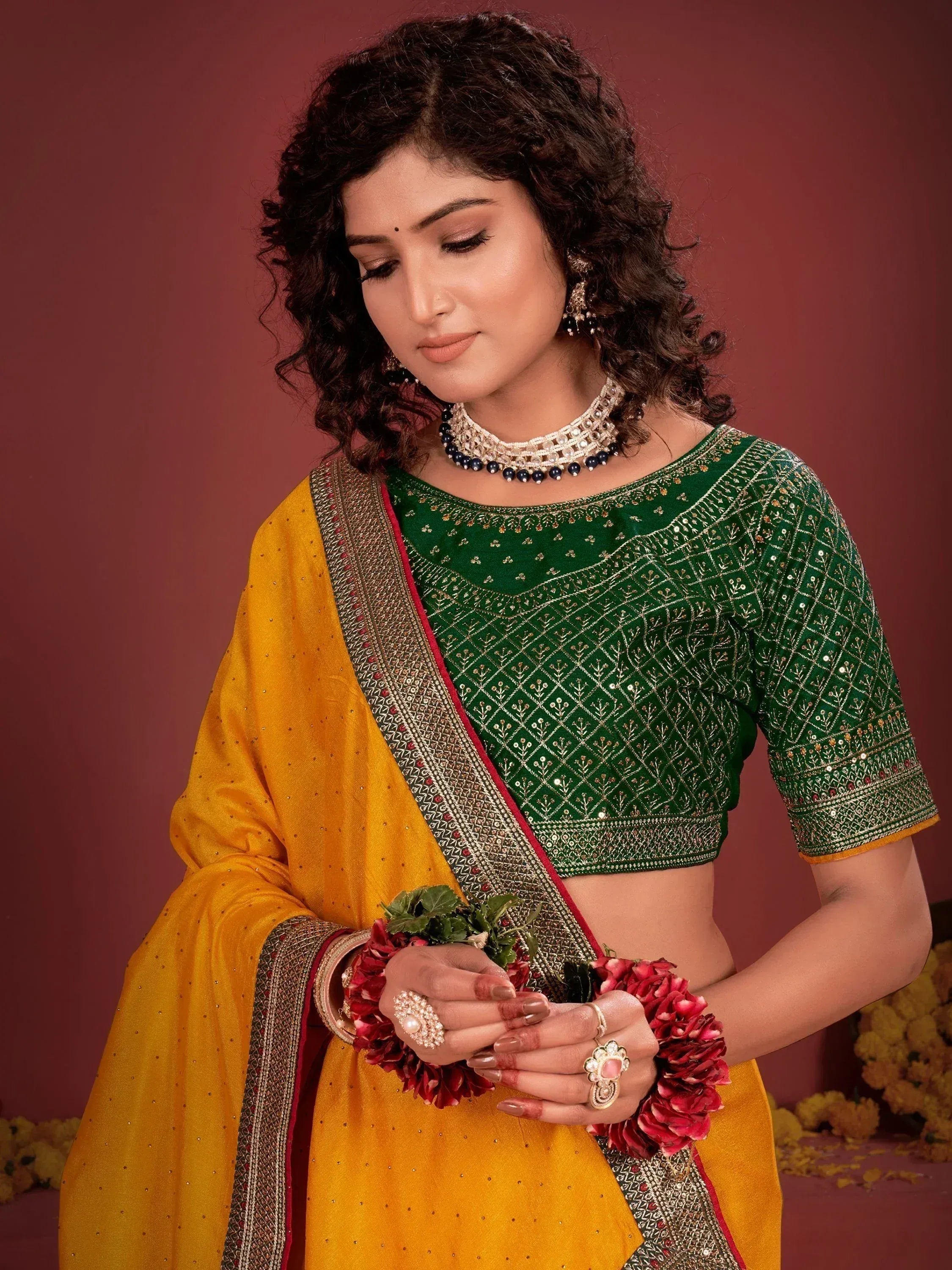 Woman in green embroidered blouse with yellow saree, floral jewelry, and traditional Indian attire