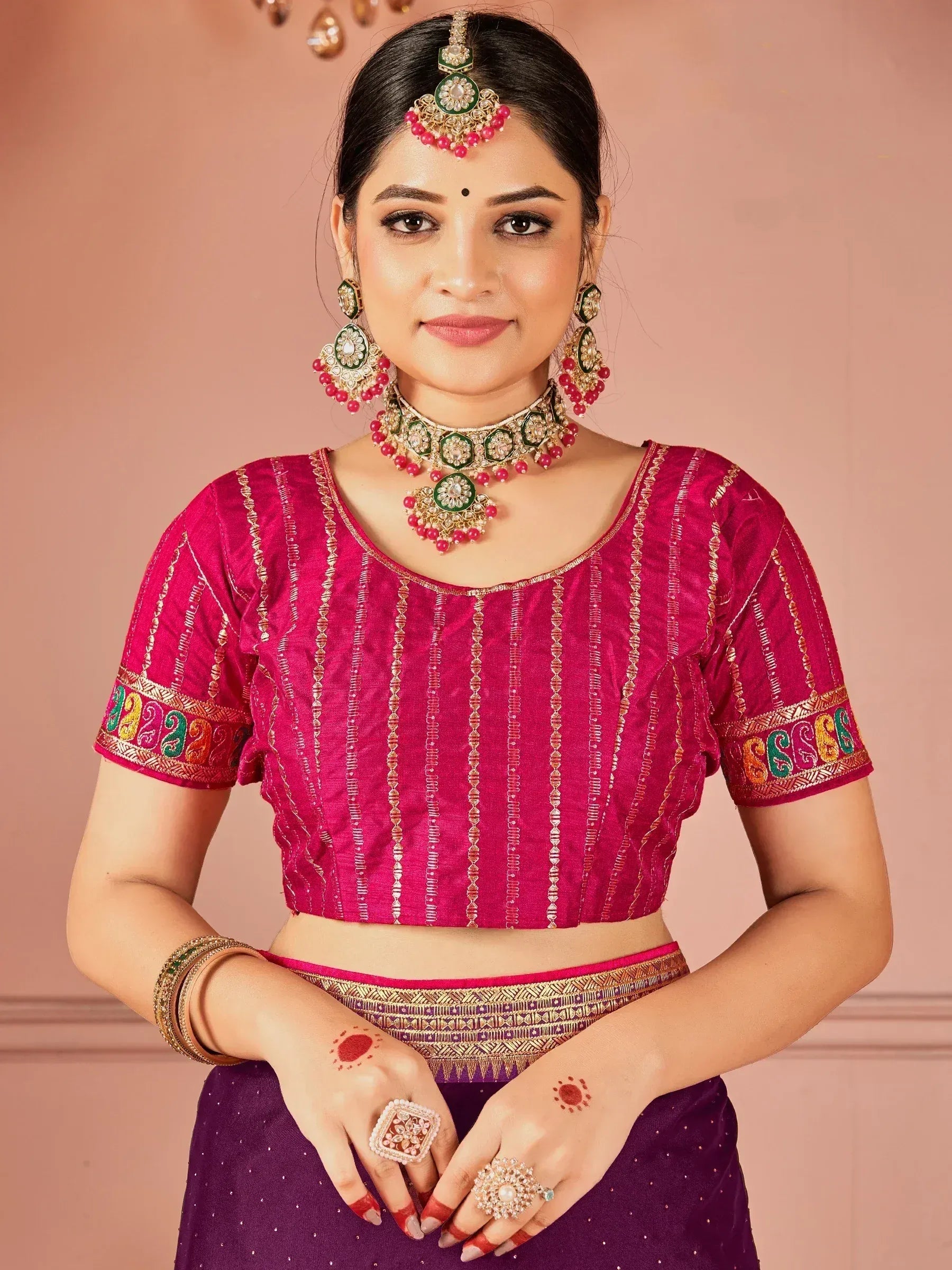Elegant Indian ethnic wear with pink embroidered blouse and purple skirt, adorned with traditional jewelry.