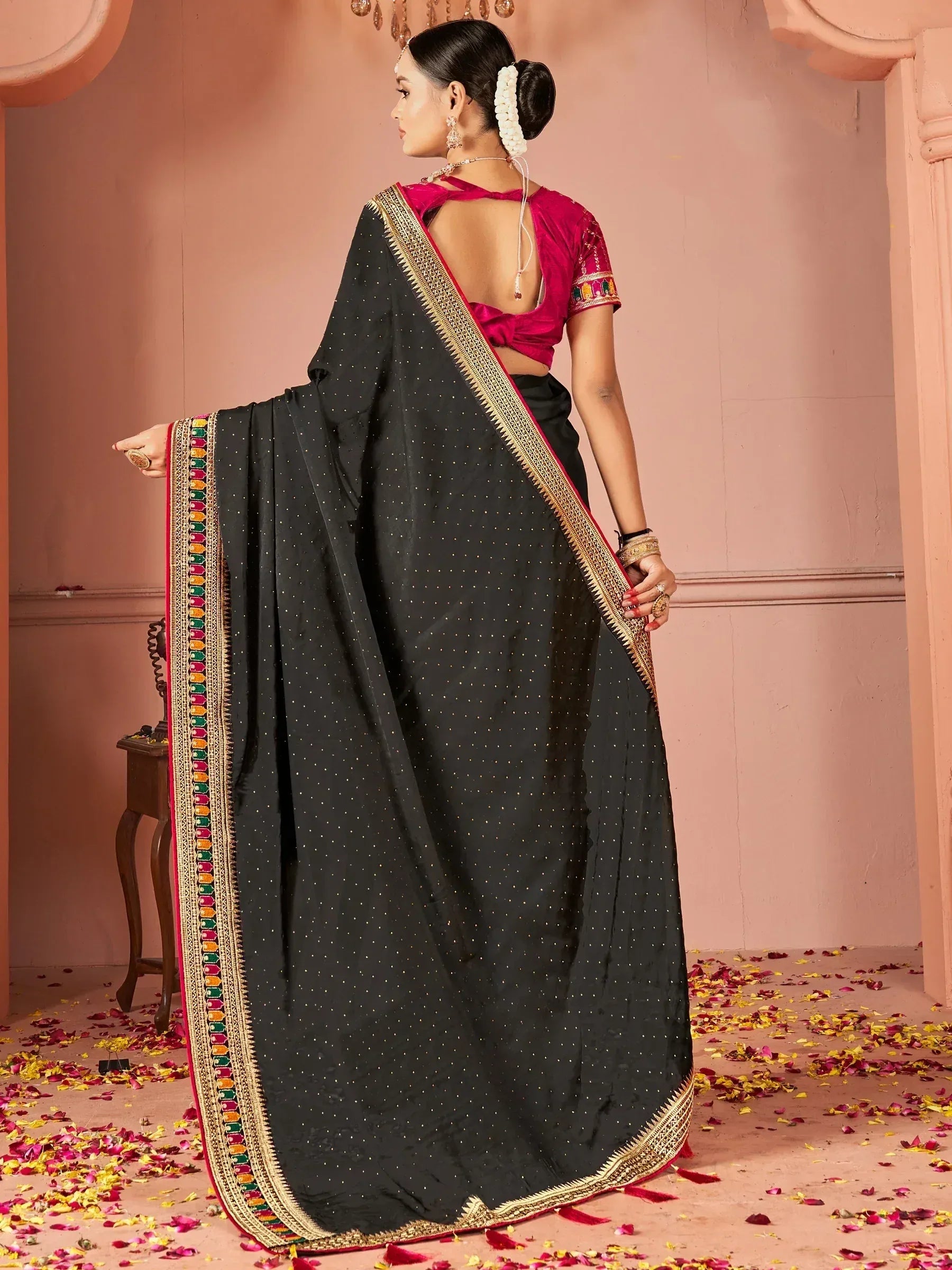 Black saree with gold polka dots and colorful border, paired with pink blouse, ideal for ethnic occasions.