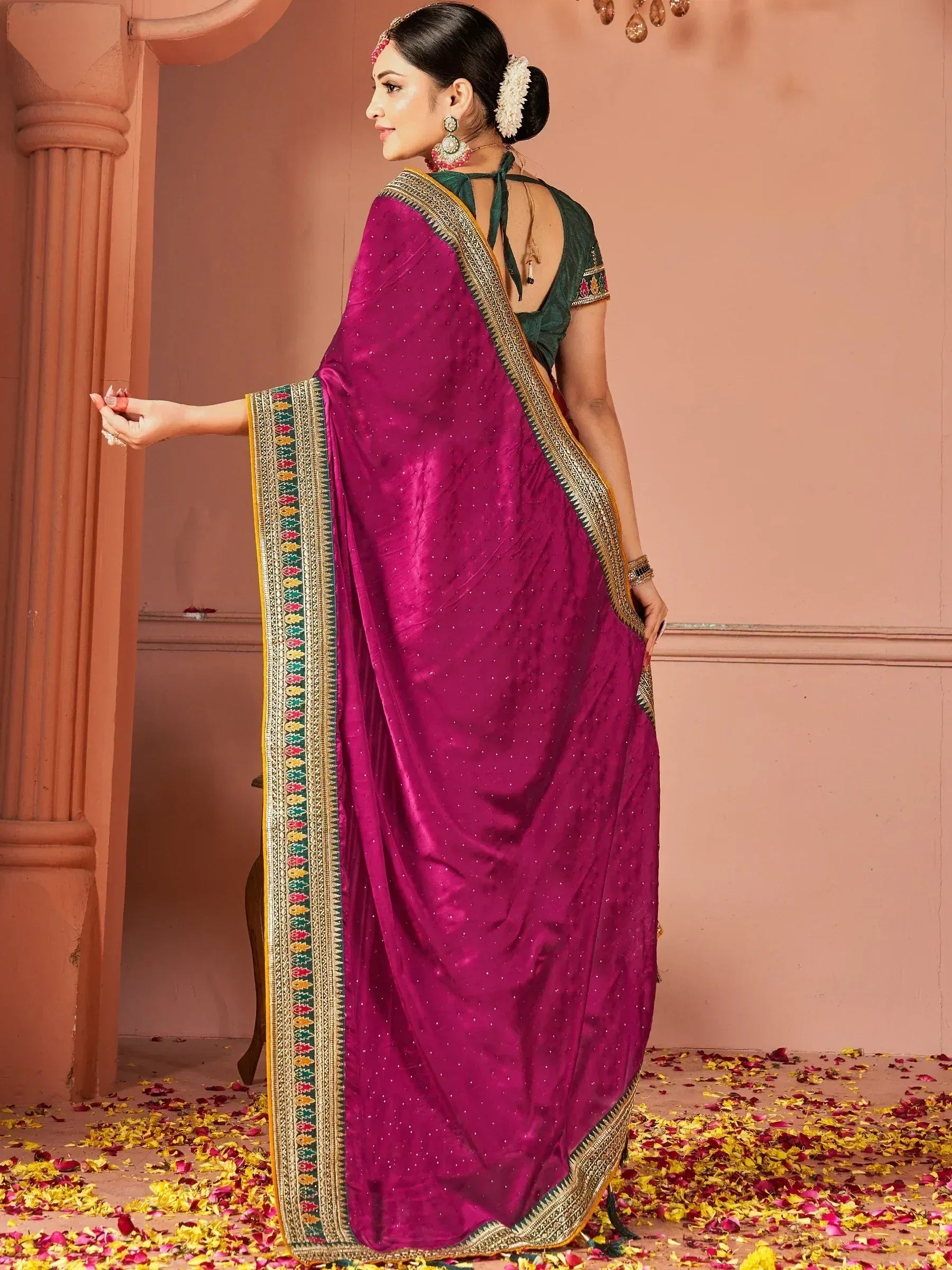 Woman in magenta ethnic saree with gold border and green blouse, floral petals on floor