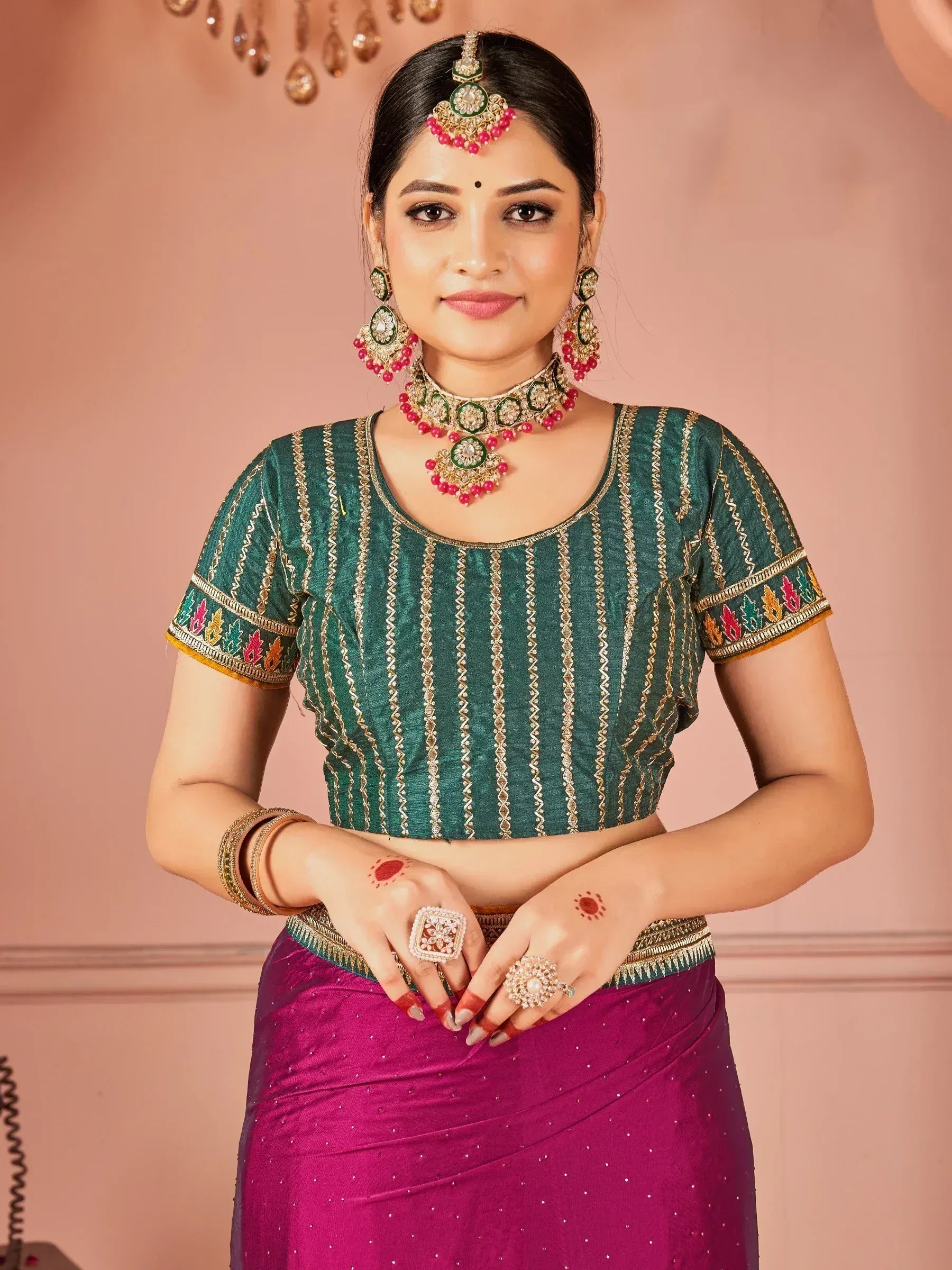 Woman in green embroidered blouse and magenta saree with traditional Indian jewelry
