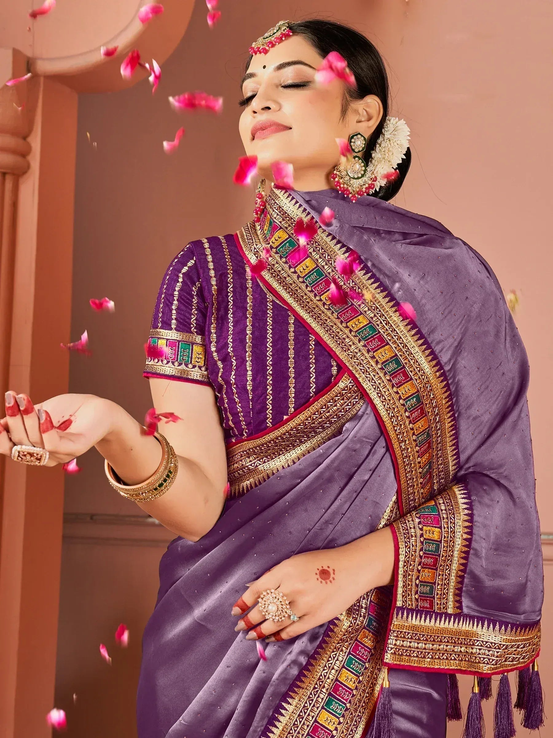 Purple designer saree with gold embroidery, floral petals, traditional jewelry, and festive ethnic wear styling