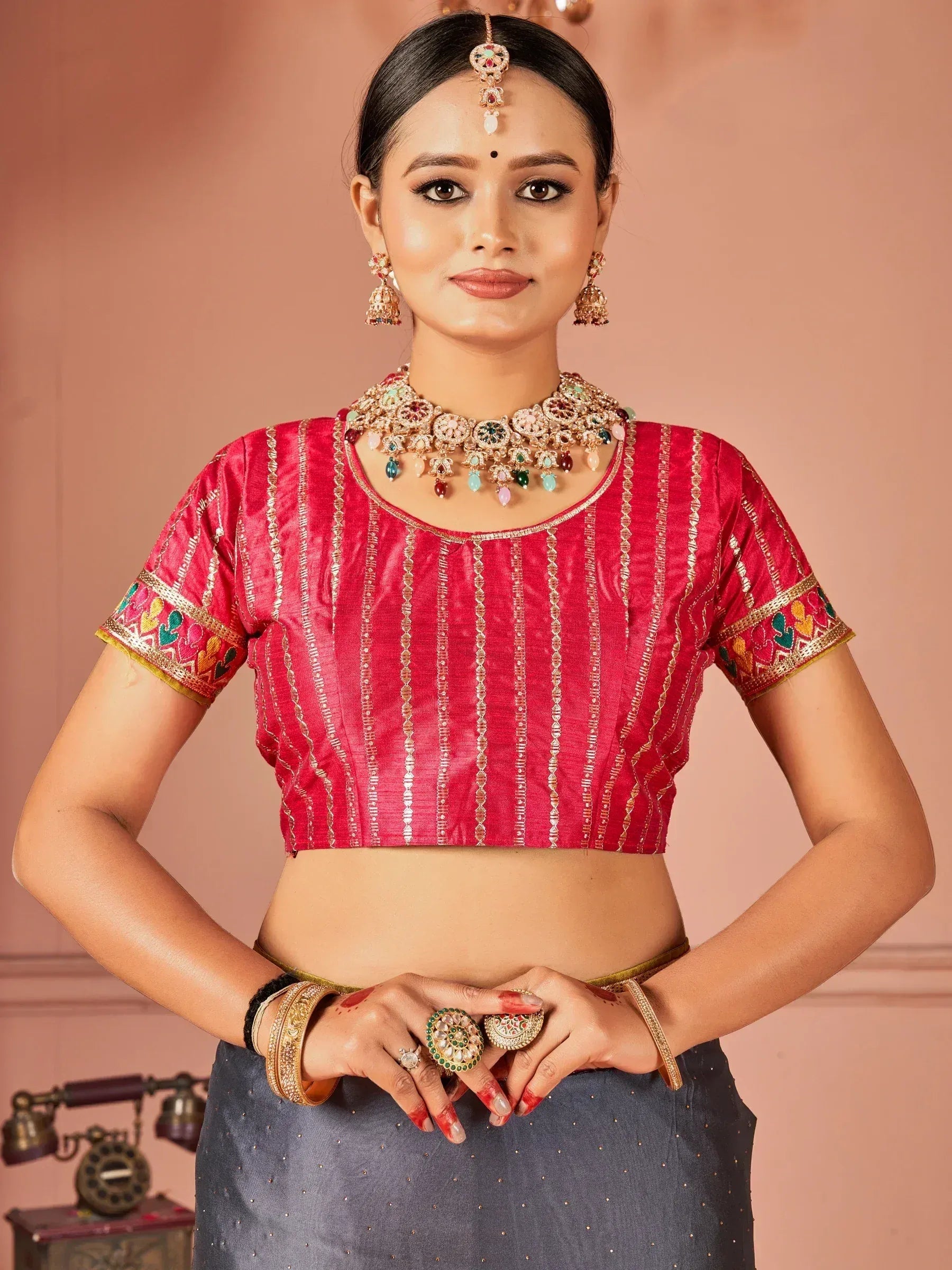 Red embroidered blouse with gold detailing, paired with traditional Indian jewelry and grey skirt