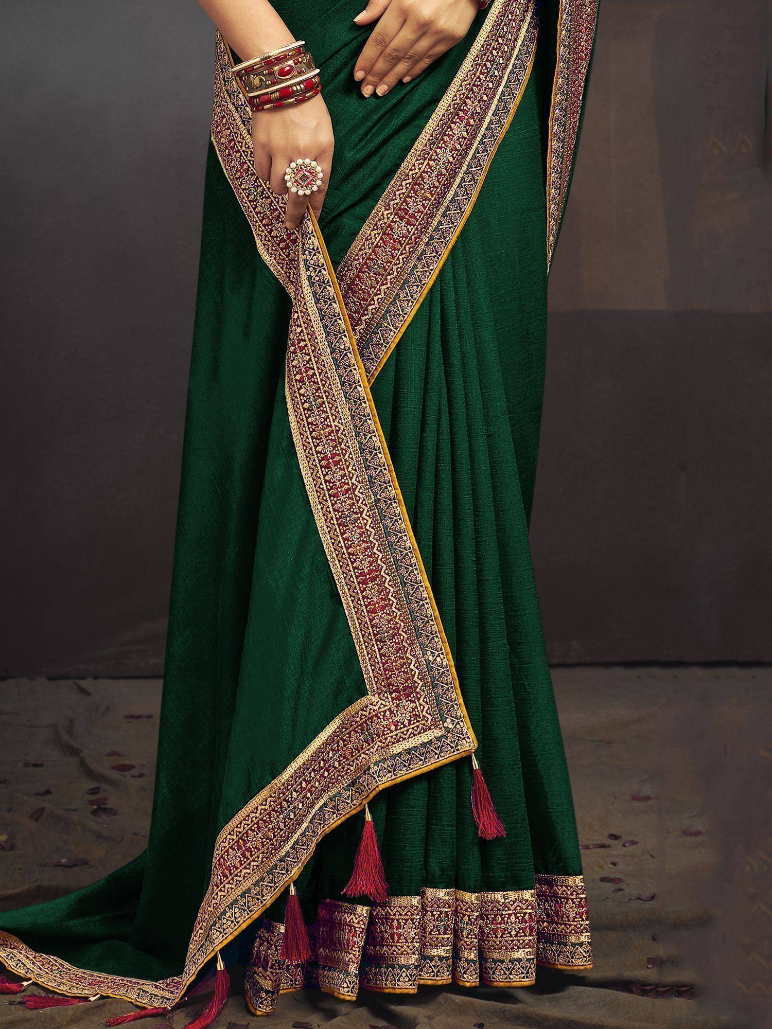 Emerald green designer saree with intricate gold and red border, tassels, and traditional Indian embroidery.