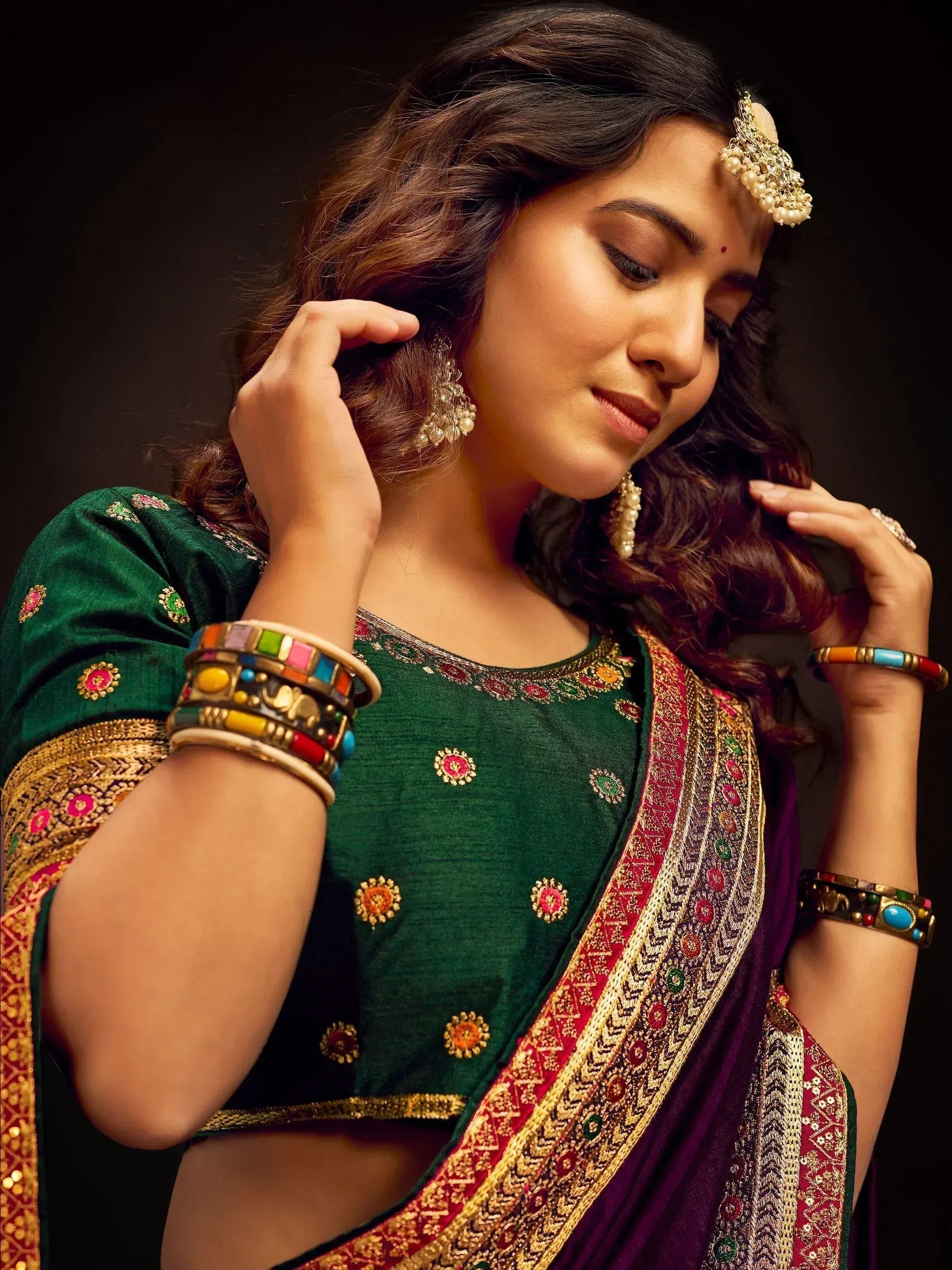 Woman in green embroidered blouse and purple saree with gold border, wearing traditional Indian jewelry