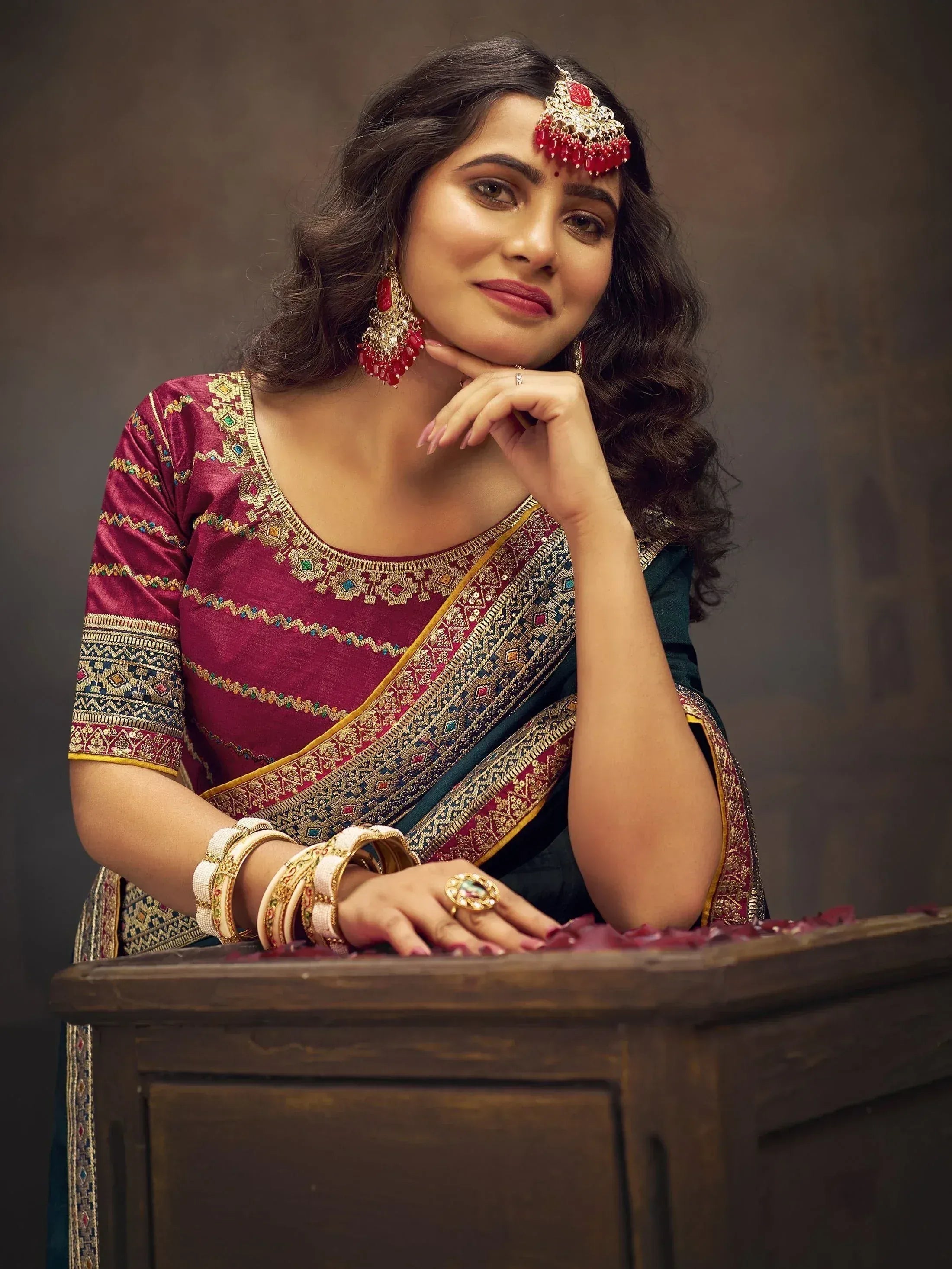 Woman in maroon and green embroidered saree with traditional jewelry, perfect for Indian ethnic wear occasions