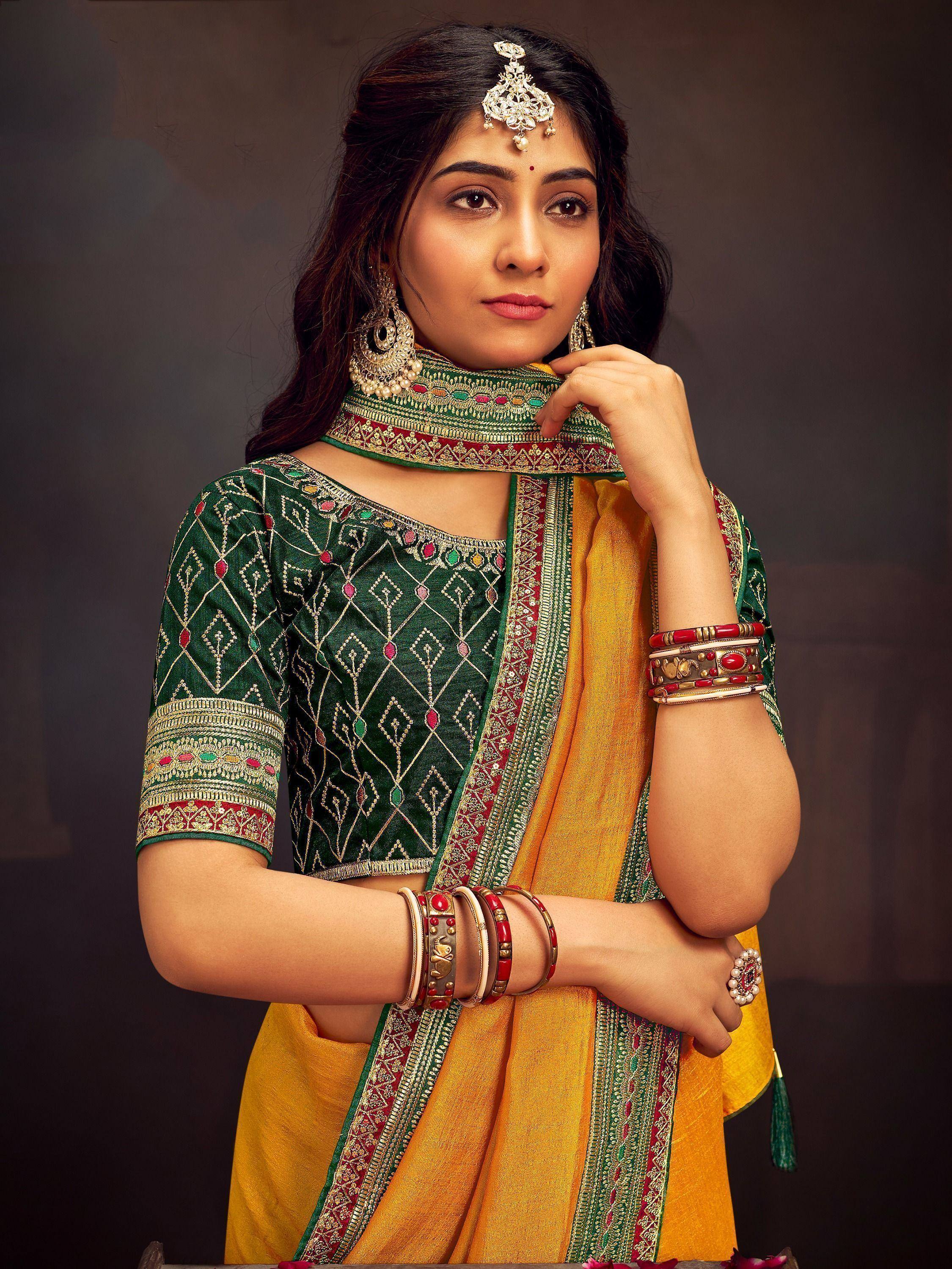 Woman in green embroidered blouse and yellow saree with traditional Indian jewelry