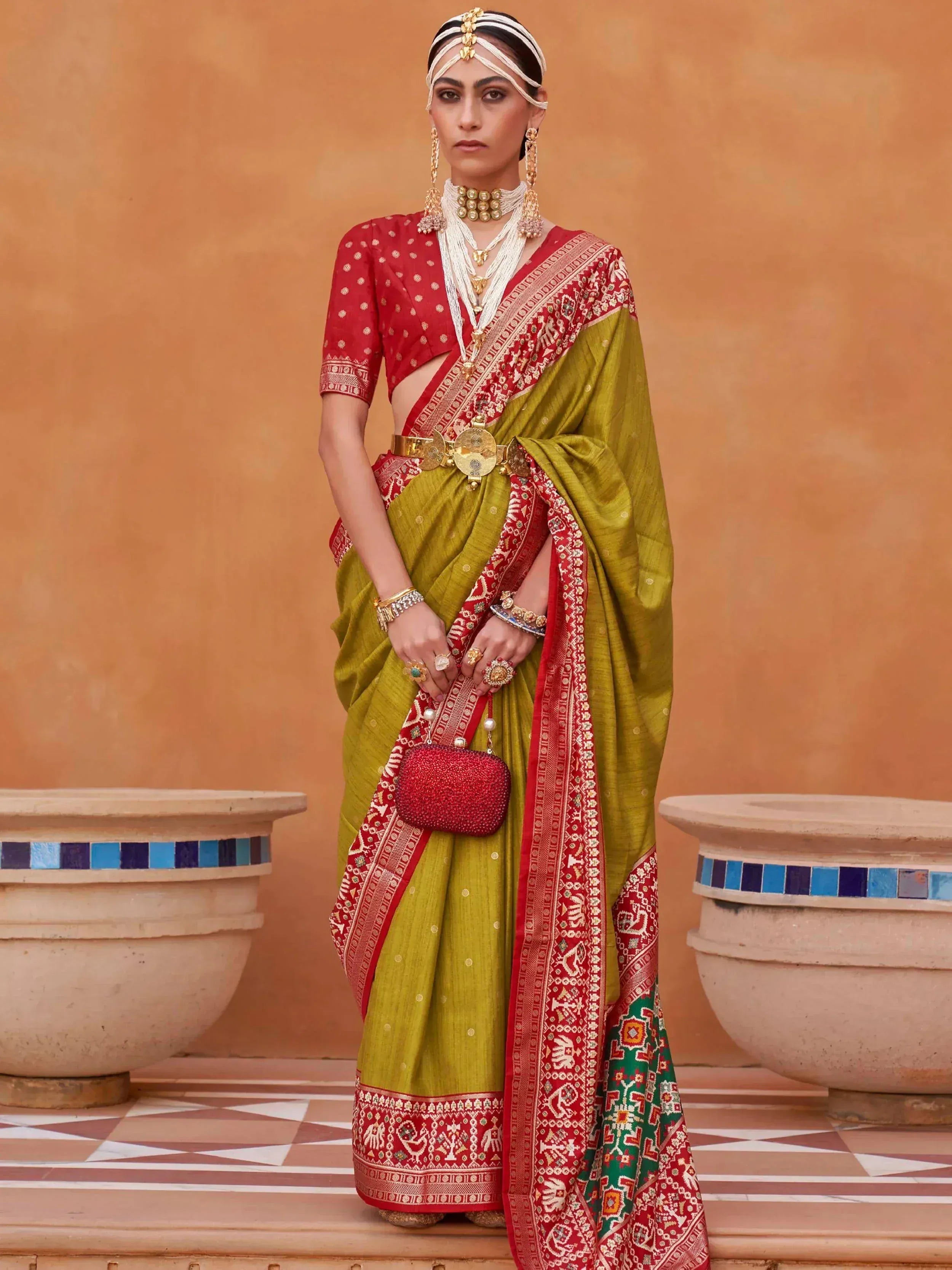 Woman in olive green and red ethnic saree with gold jewelry and traditional headpiece
