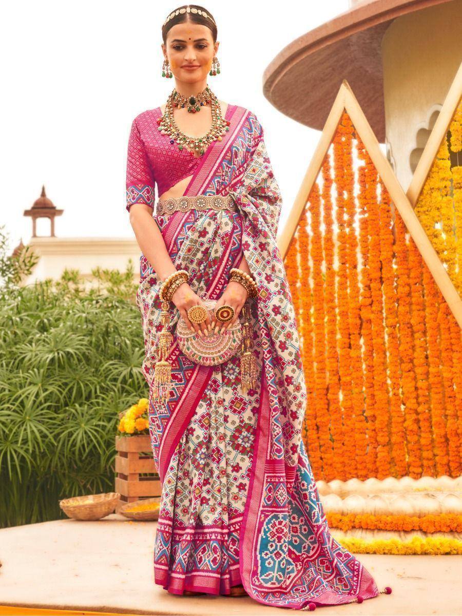Woman in vibrant printed saree with pink blouse, traditional jewelry, and floral backdrop