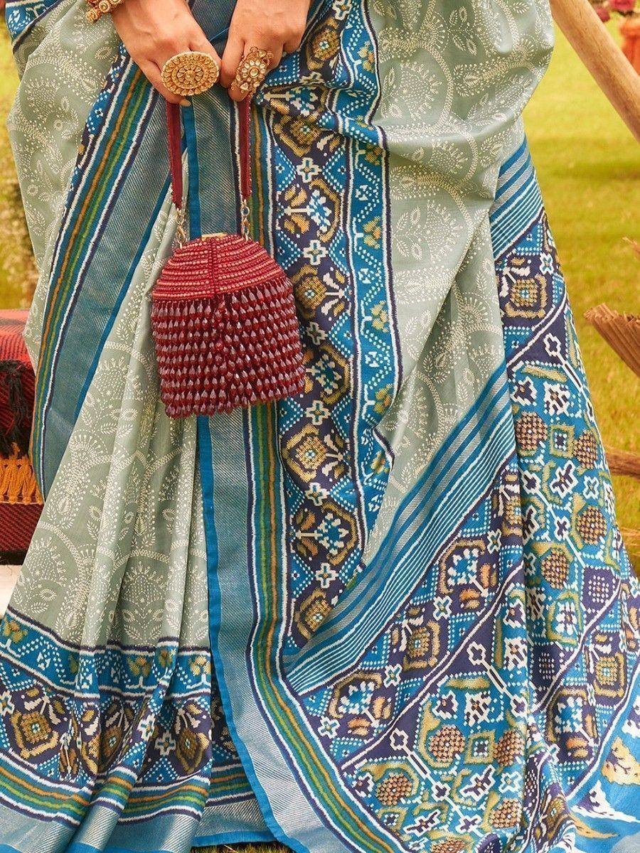 Women's ethnic saree with blue and green printed border, paired with red beaded potli bag and gold jewelry