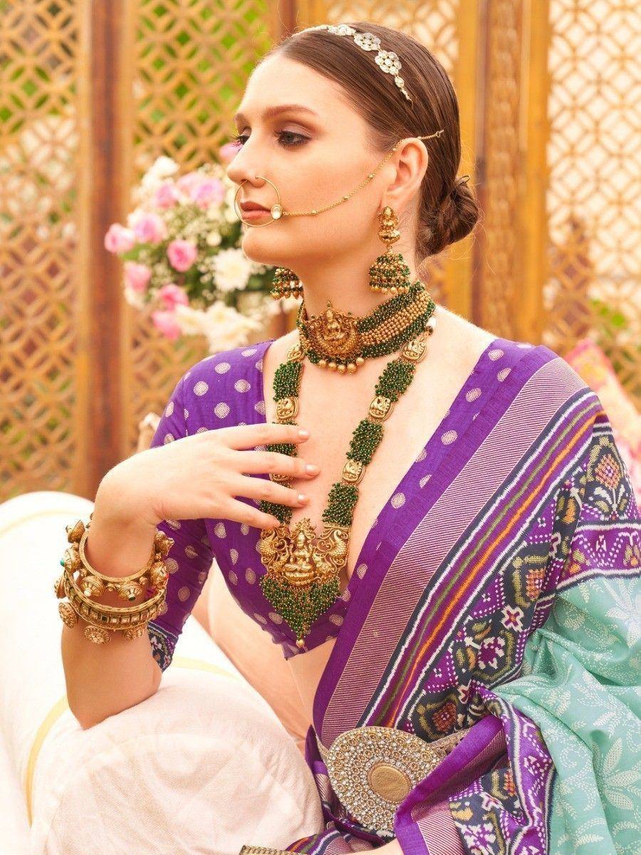Woman in purple ethnic saree with green gold jewelry, traditional Indian attire for weddings or festivals