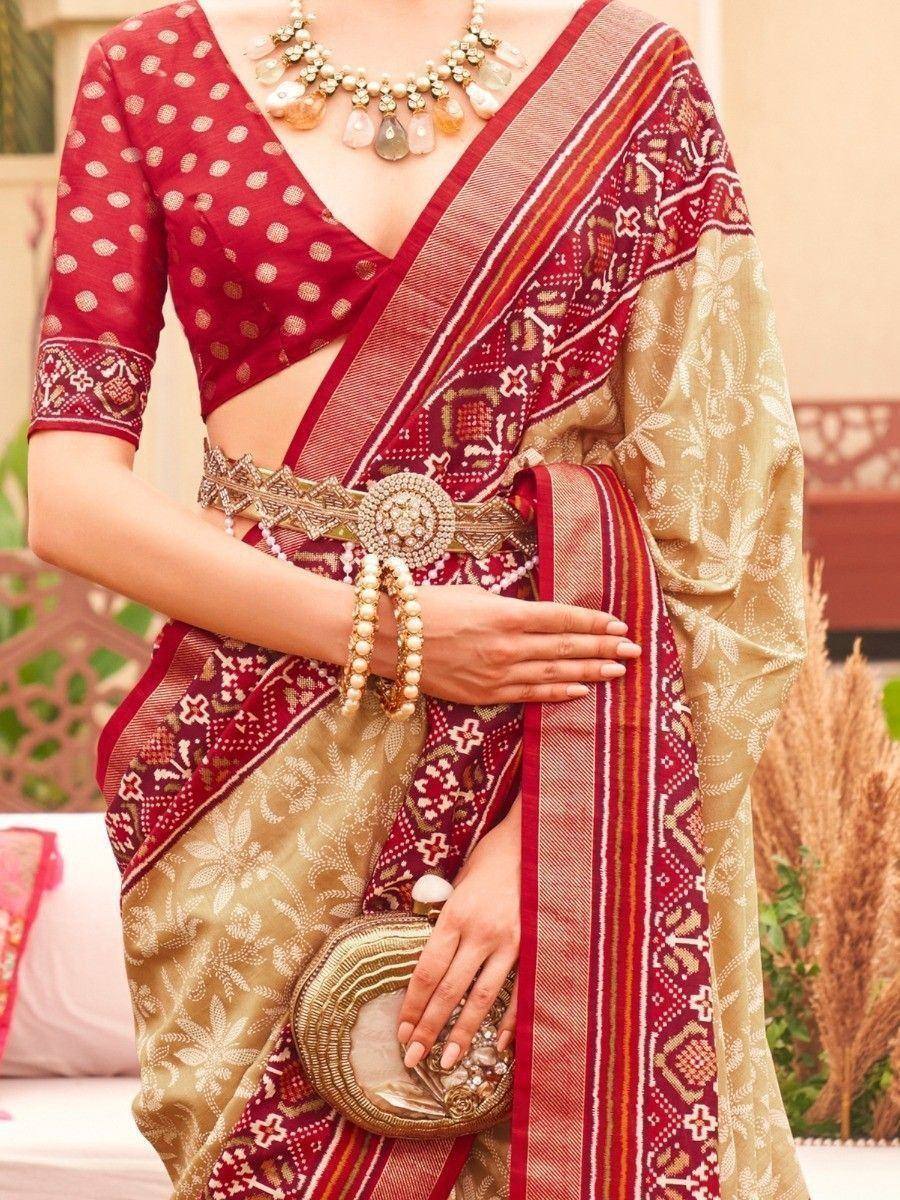 Red and gold ethnic saree with intricate patterns, paired with designer jewelry and a clutch.