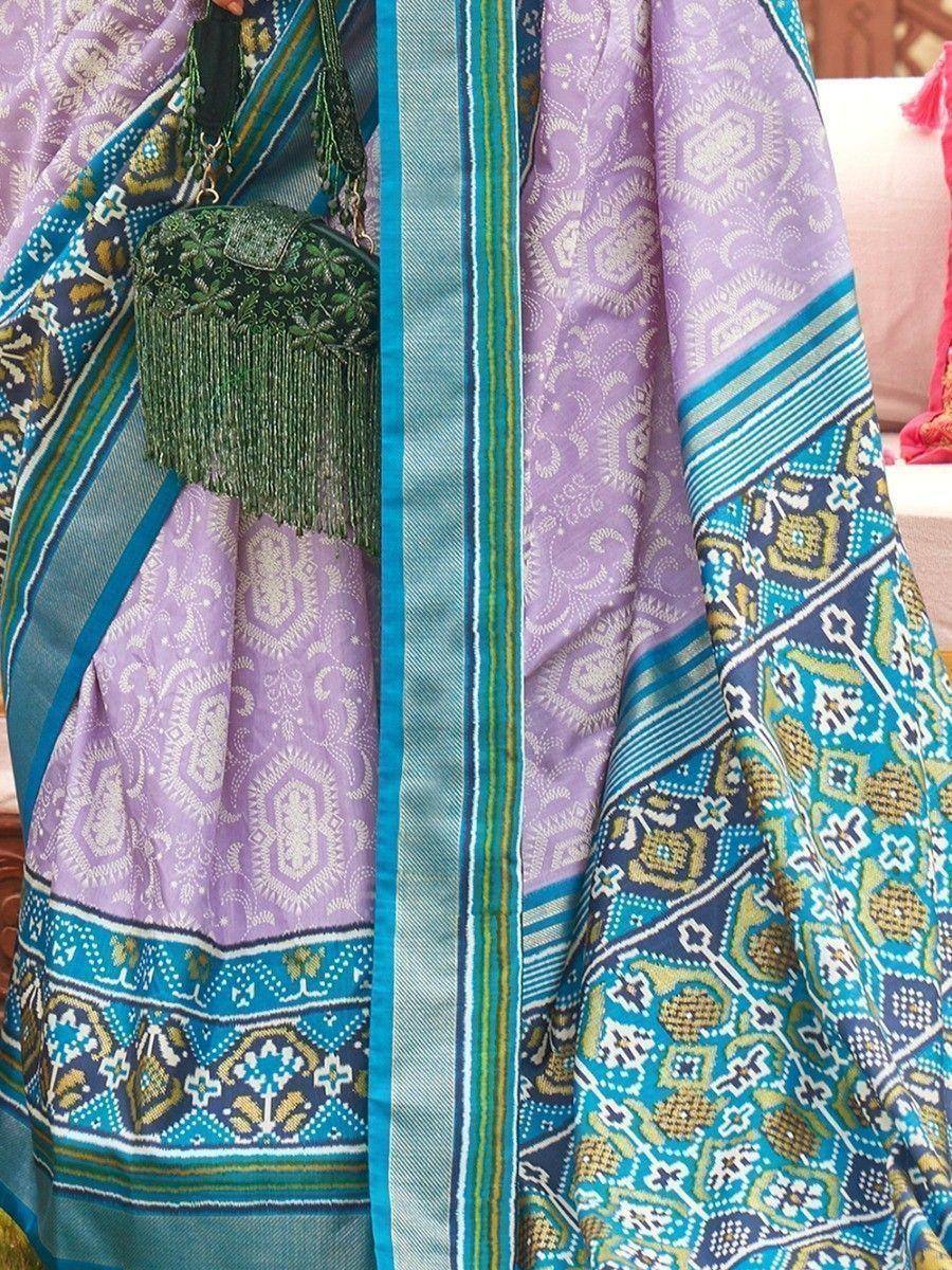 Purple and teal ethnic saree with intricate paisley and geometric patterns, paired with a green embroidered clutch.