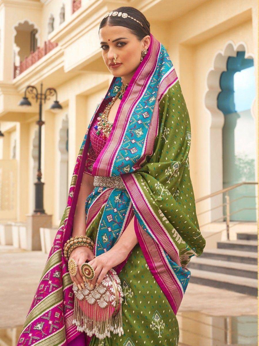 Woman in vibrant green and pink ethnic saree with intricate embroidery, traditional jewelry, and ornate clutch