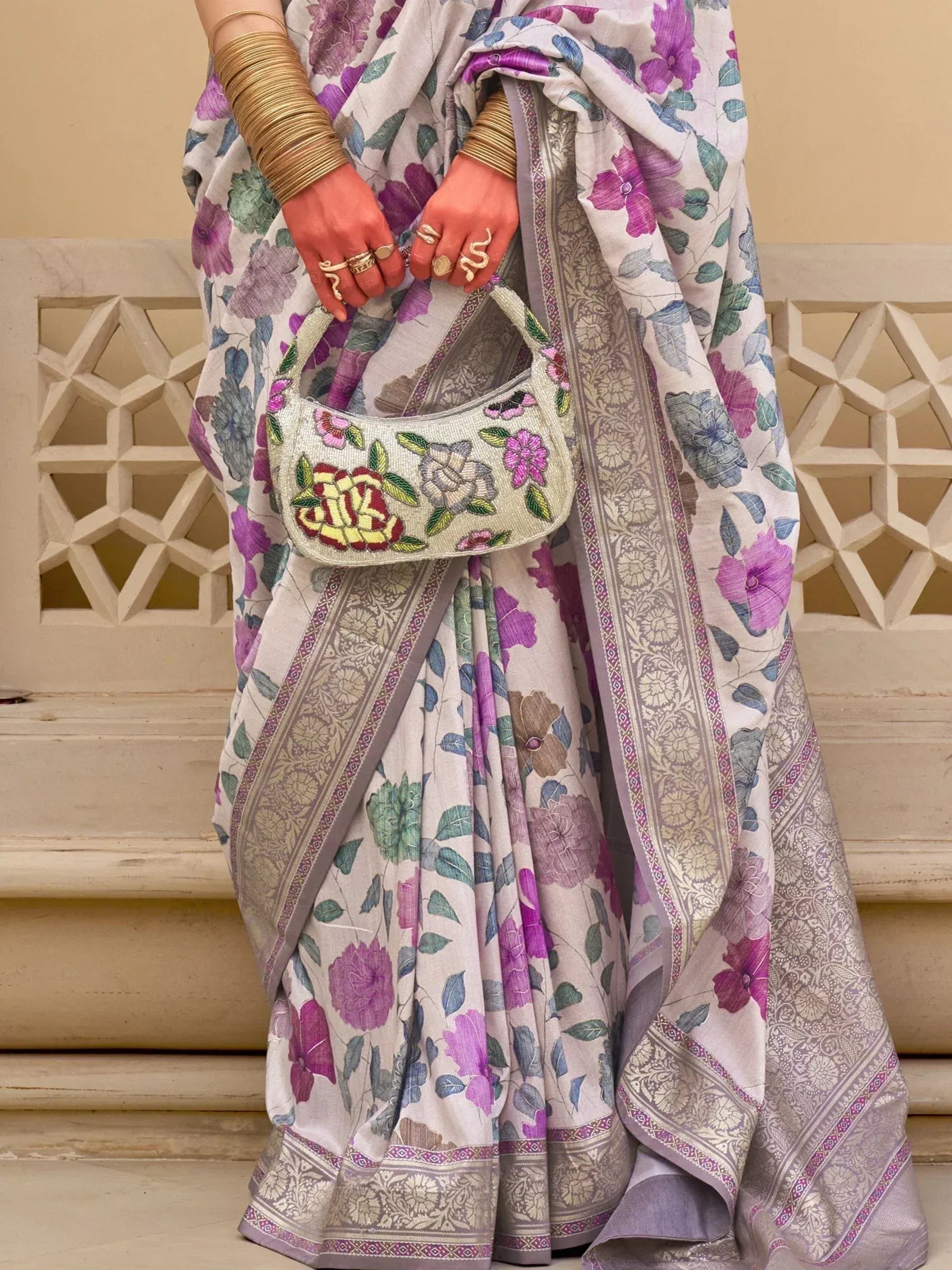 Floral print saree with embroidered border and matching handbag, styled with gold bangles and rings