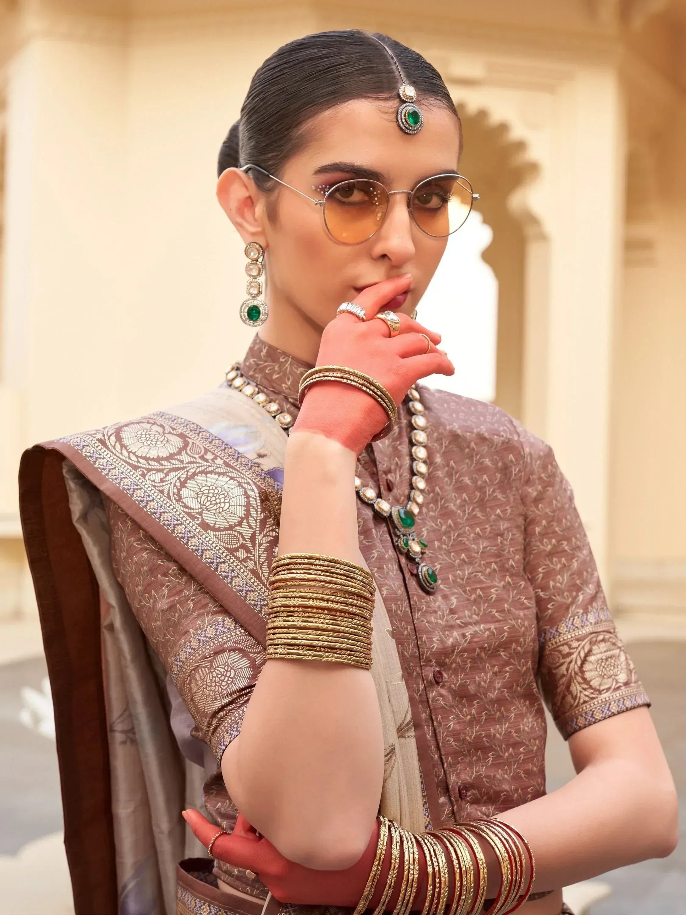Woman in traditional Indian saree with intricate embroidery, emerald jewelry, and stylish sunglasses