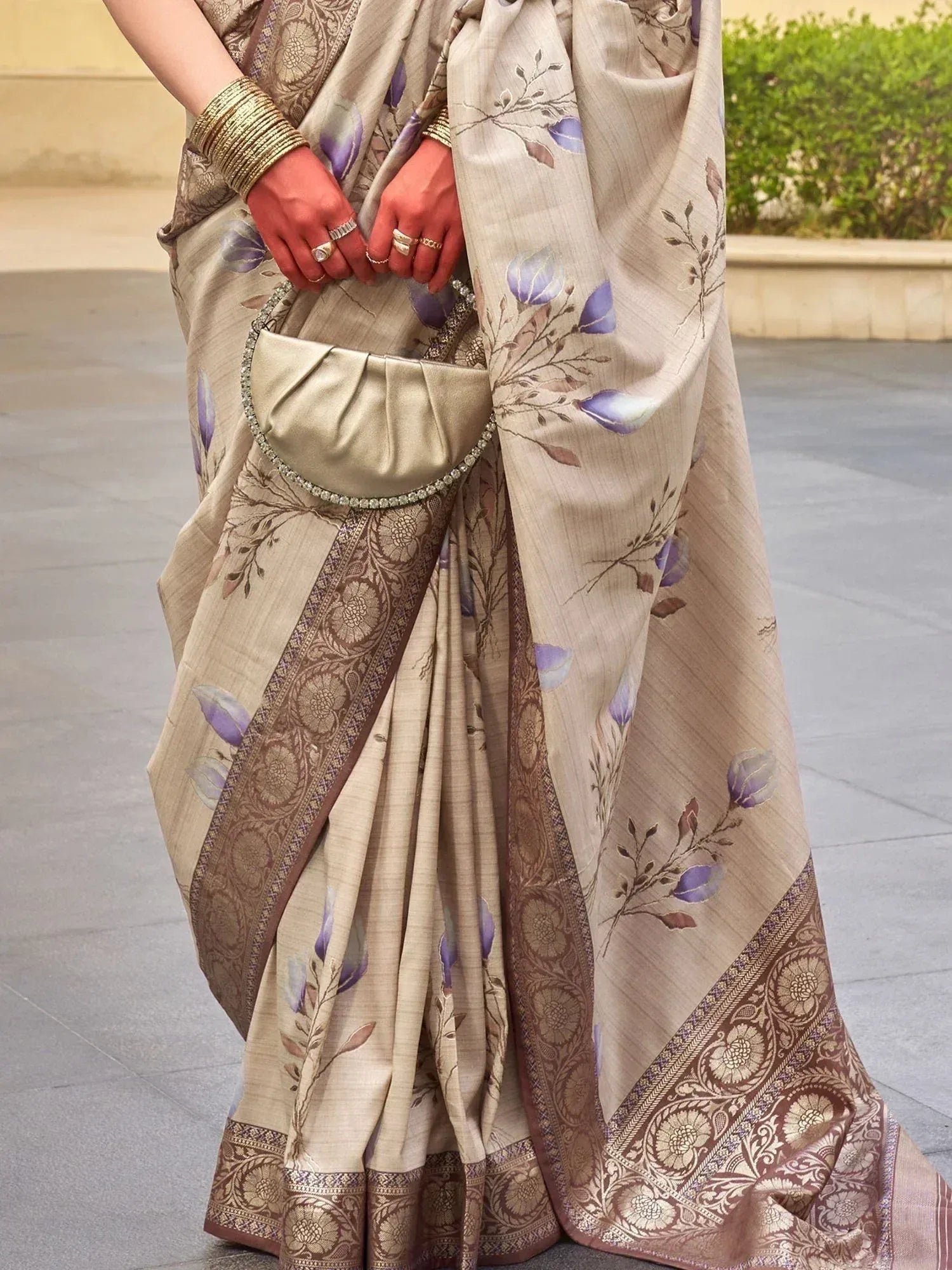 Beige floral saree with purple blooms and gold border, paired with matching clutch and bangles