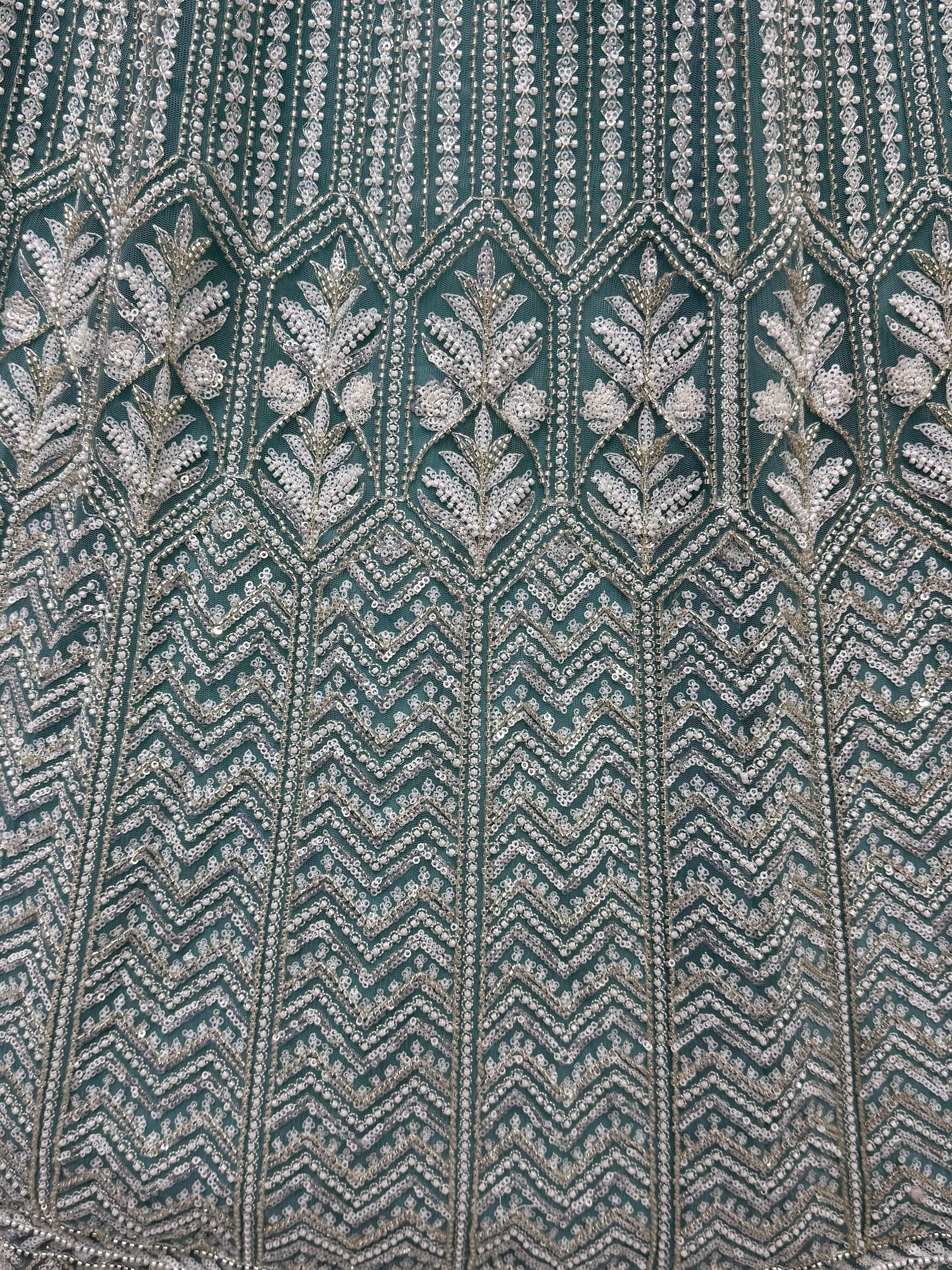 Teal ethnic wear fabric with intricate silver sequin and bead embroidery, featuring floral and geometric patterns.