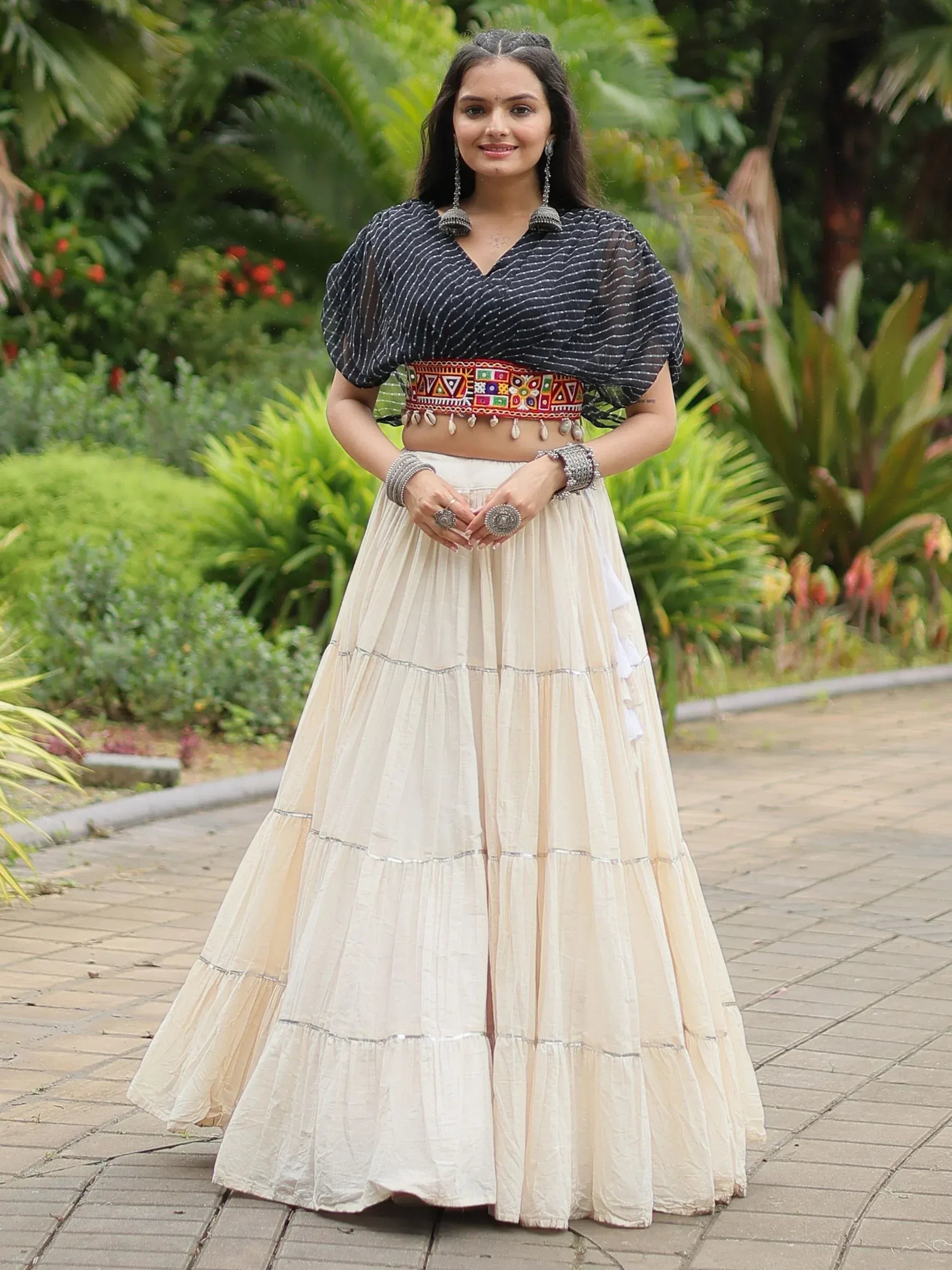 Woman in ethnic Indian lehenga choli with striped crop top and embroidered belt, garden setting