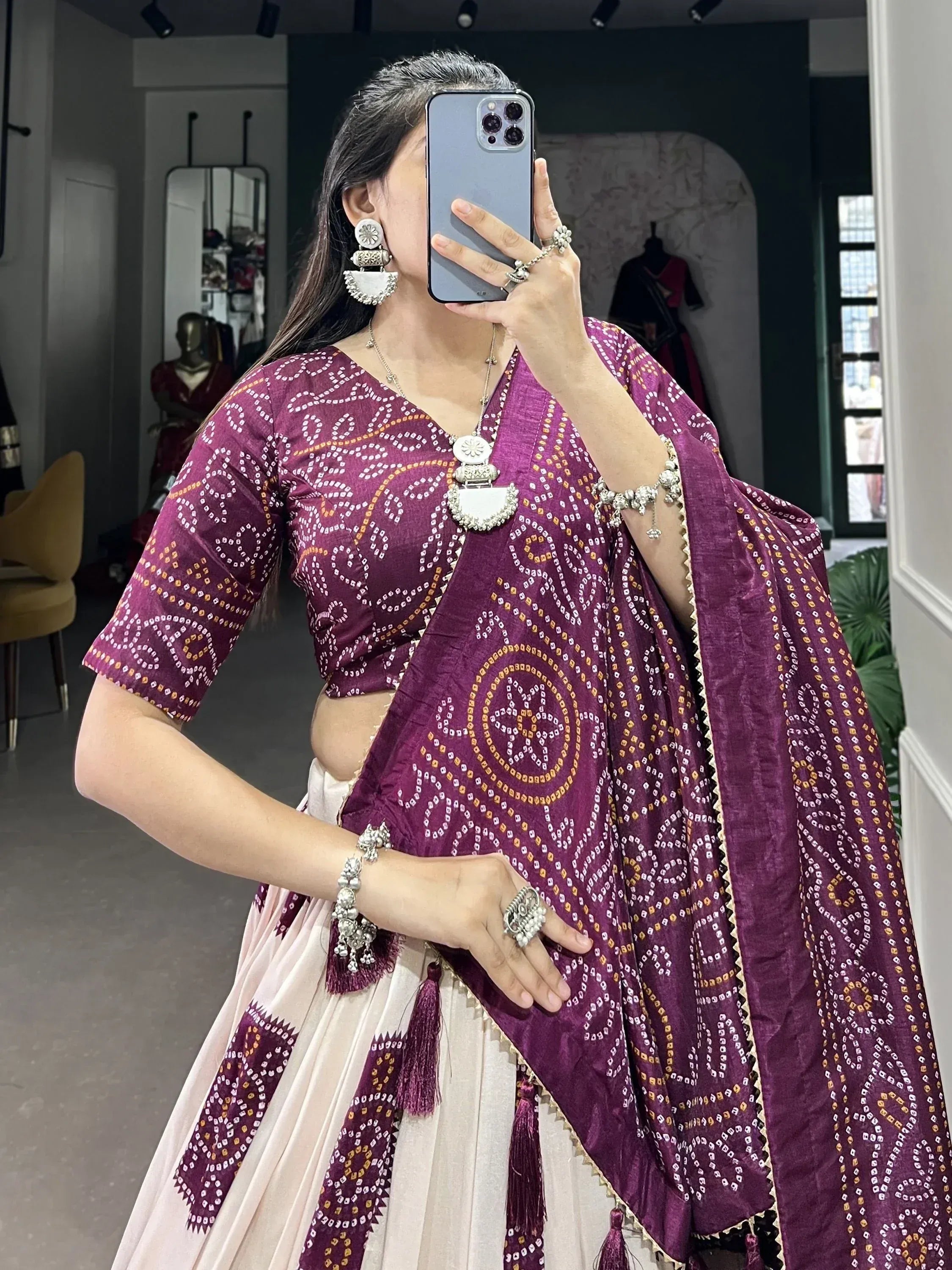 Woman in purple bandhani lehenga choli with silver jewelry, taking mirror selfie in boutique