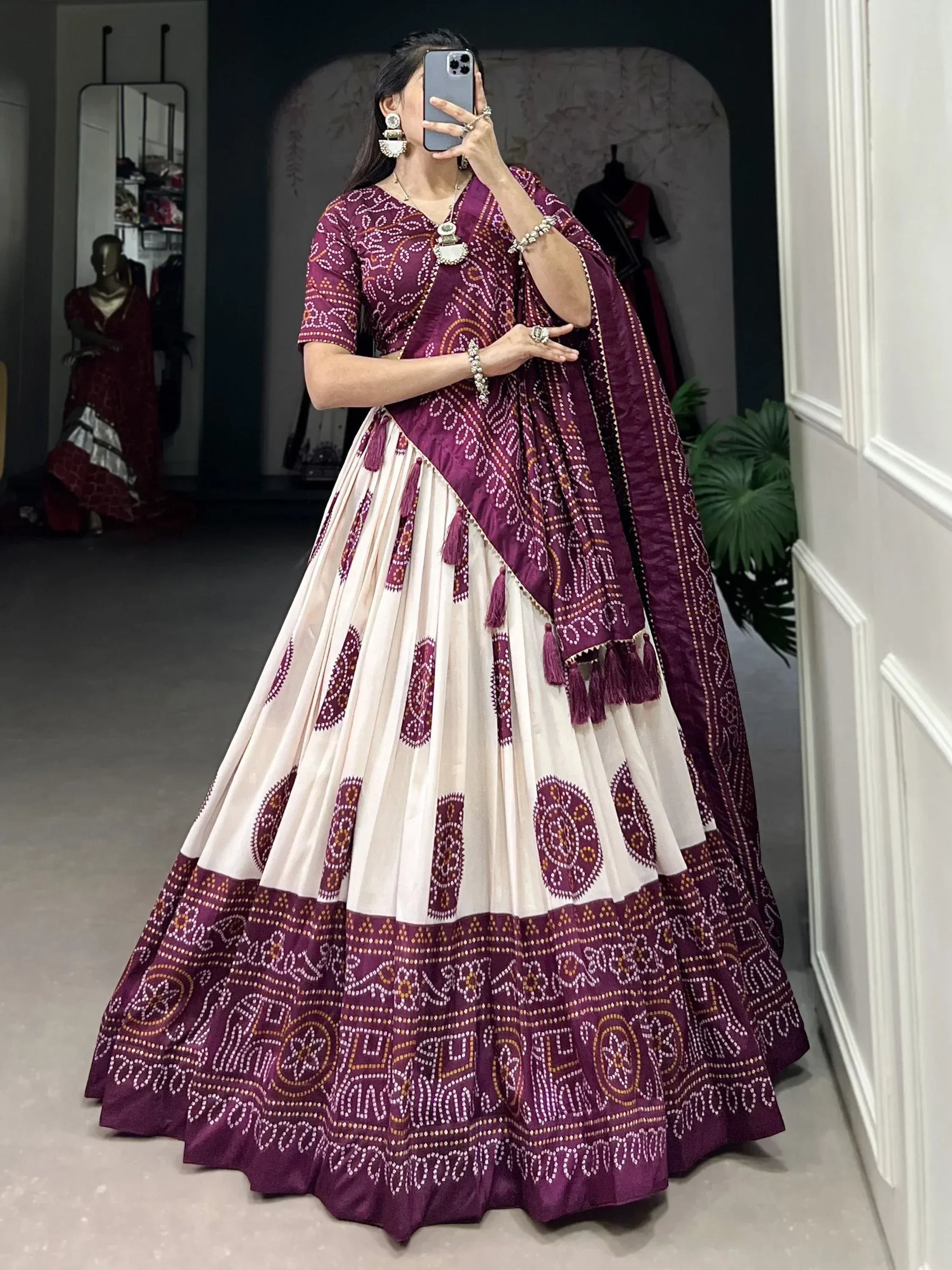 Woman in purple and cream printed lehenga choli with tassels, mirror selfie in boutique