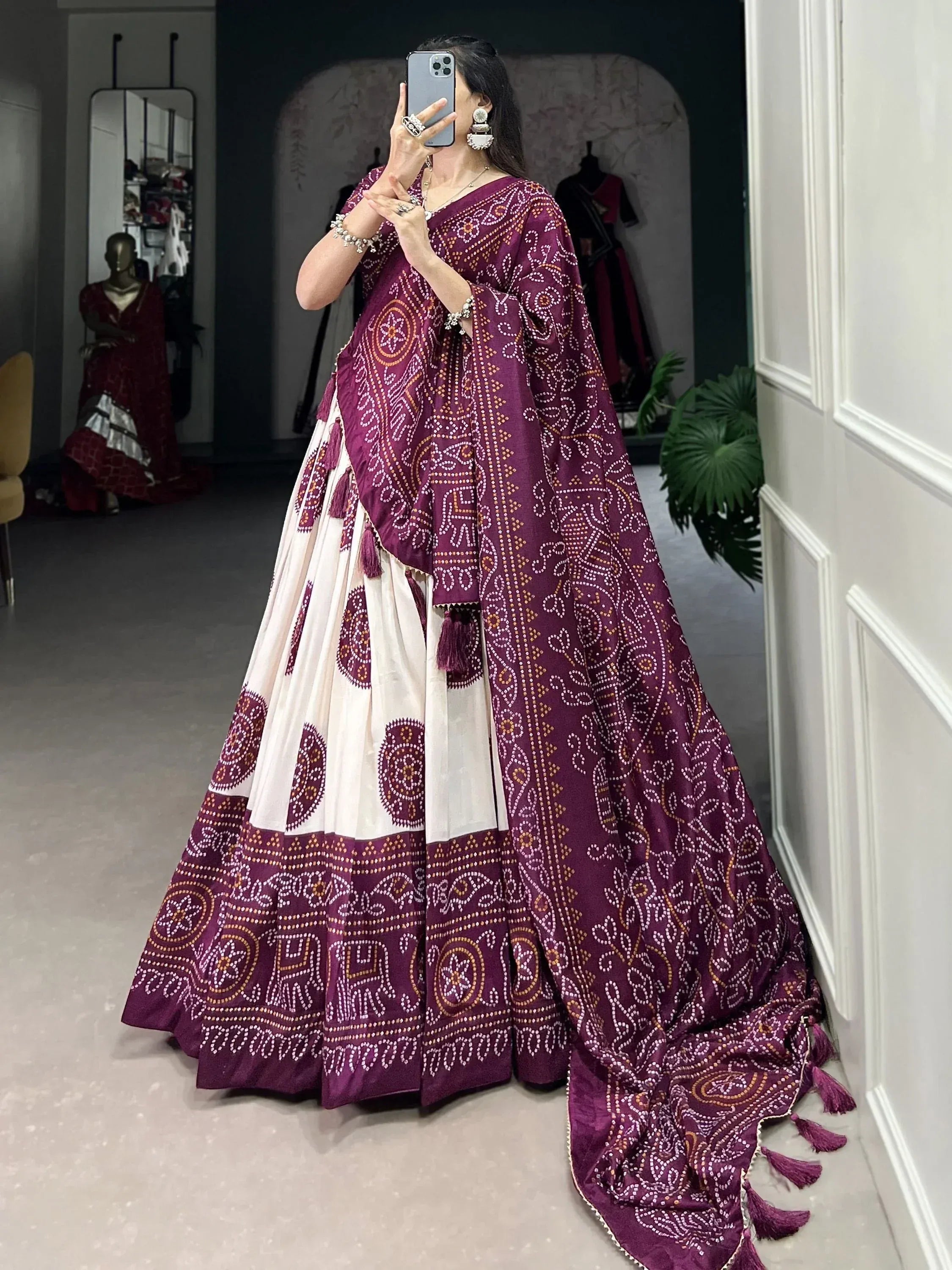 Woman in purple and white printed lehenga choli with tassels, taking mirror selfie in boutique