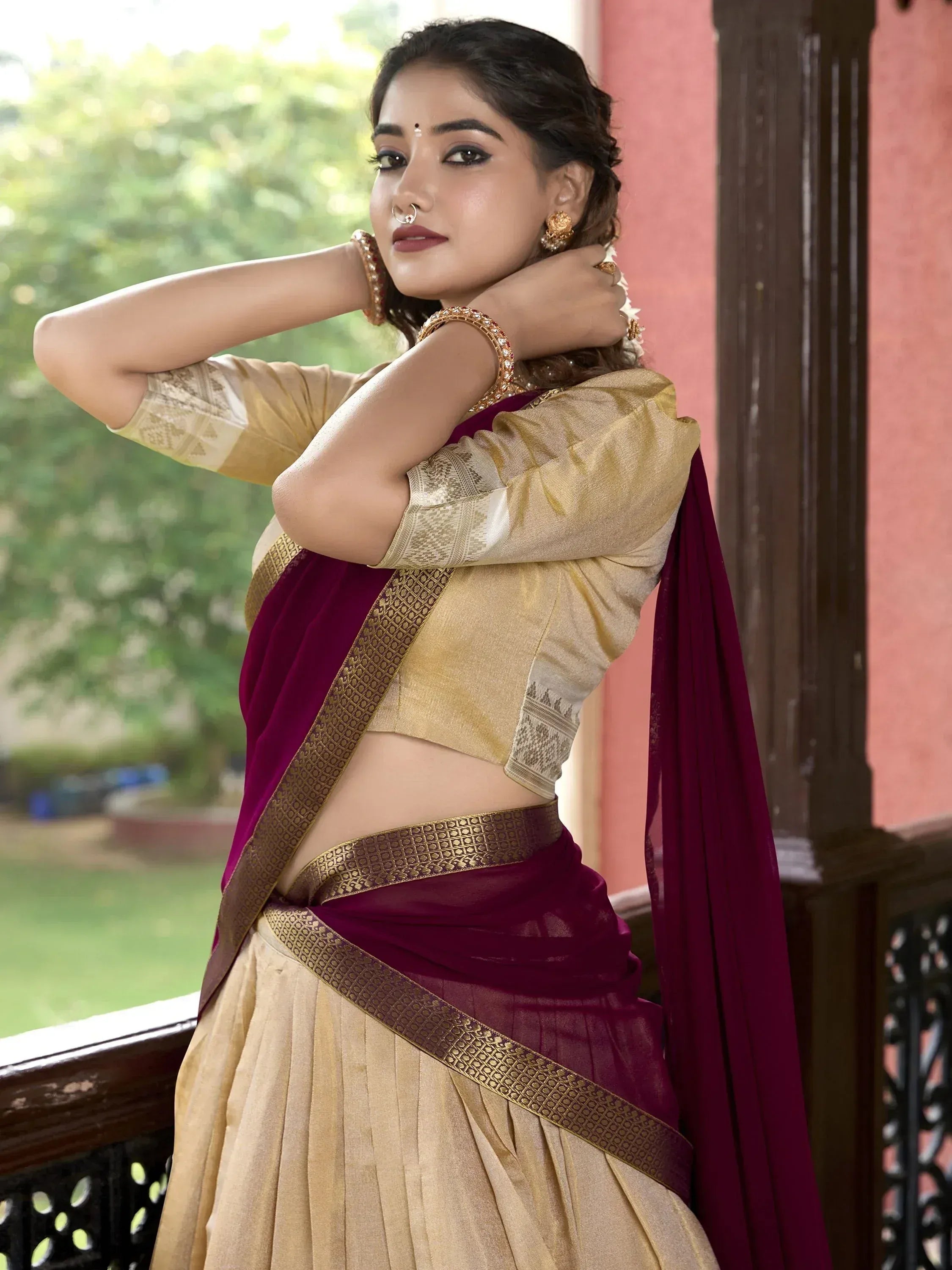 Woman in maroon and gold designer saree with ethnic jewelry, perfect for Indian occasions