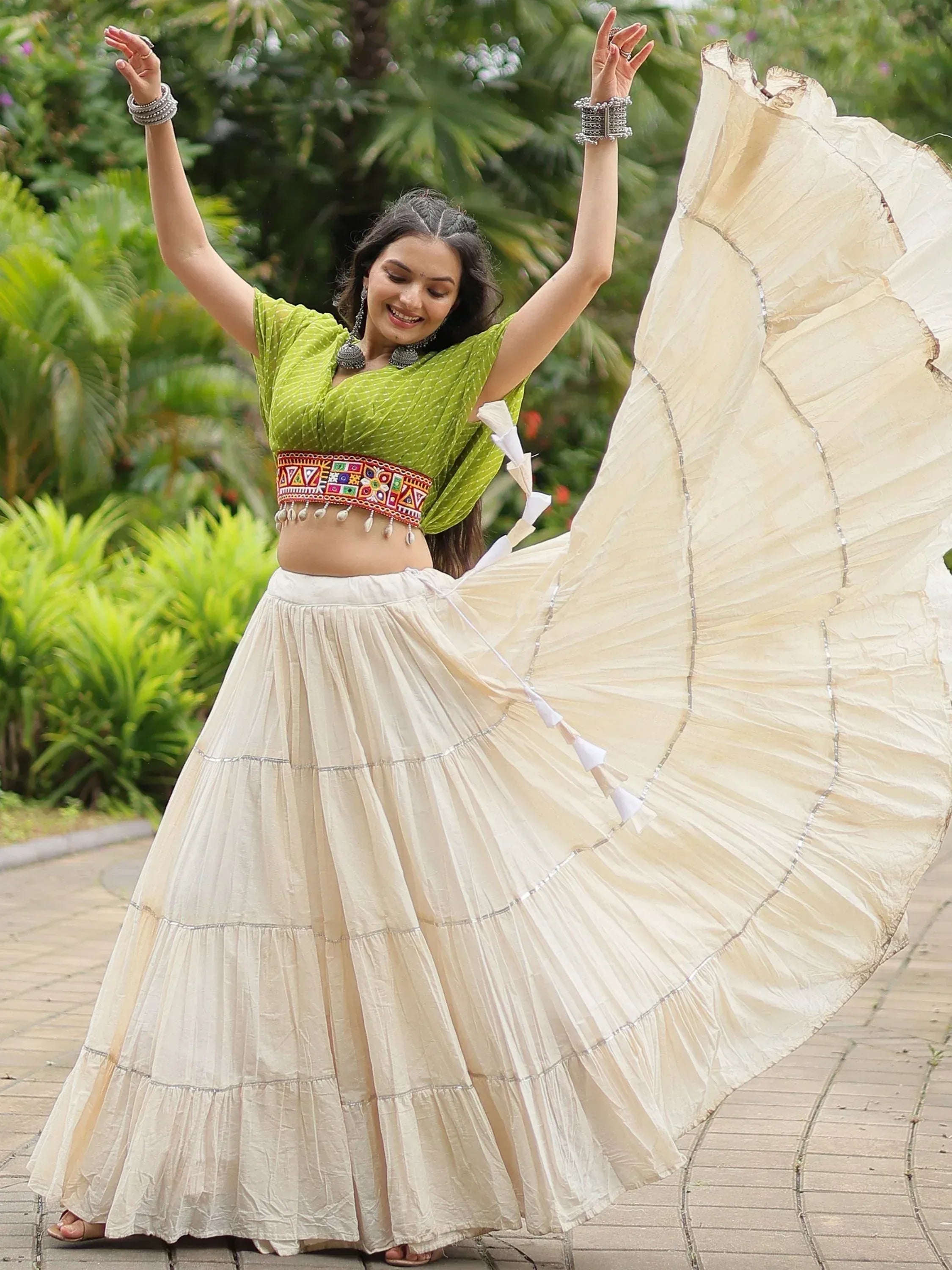 Woman dancing in green crop top and cream flared skirt, Indian ethnic wear with embroidered belt