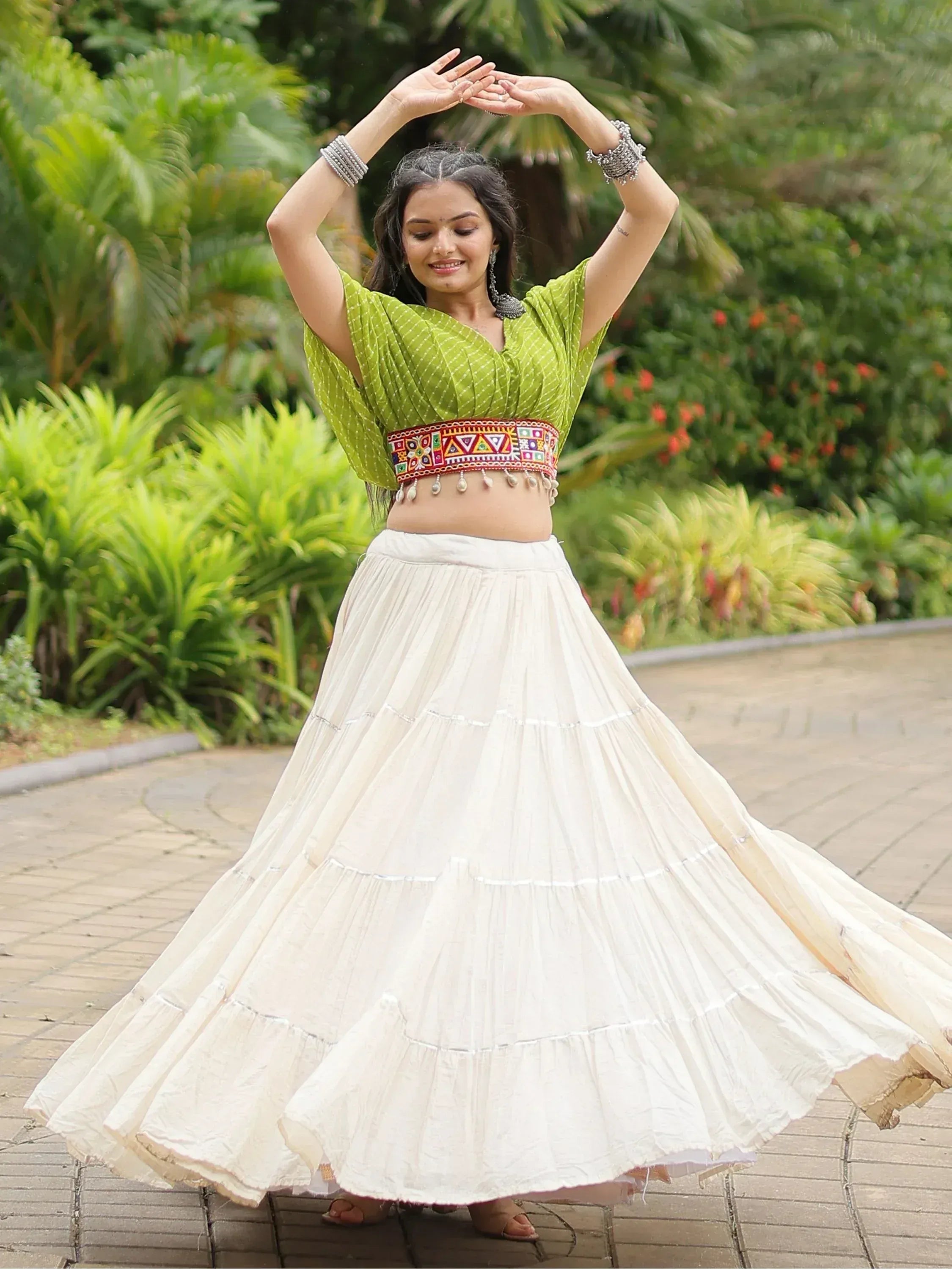 Woman in green printed crop top and white tiered skirt, dancing outdoors in ethnic wear