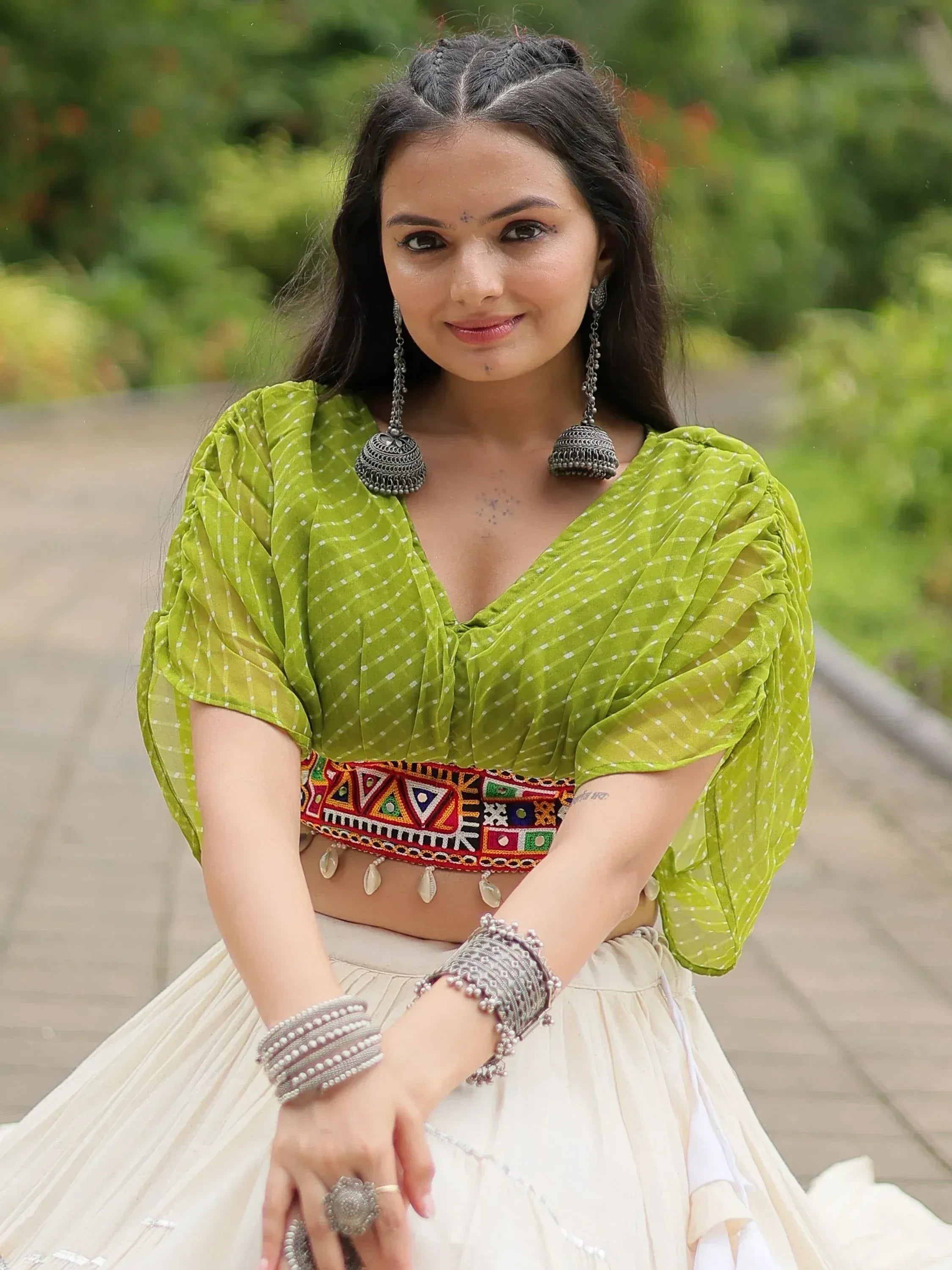 Woman in green polka dot blouse with embroidered belt, white lehenga, and silver jewelry for ethnic wear
