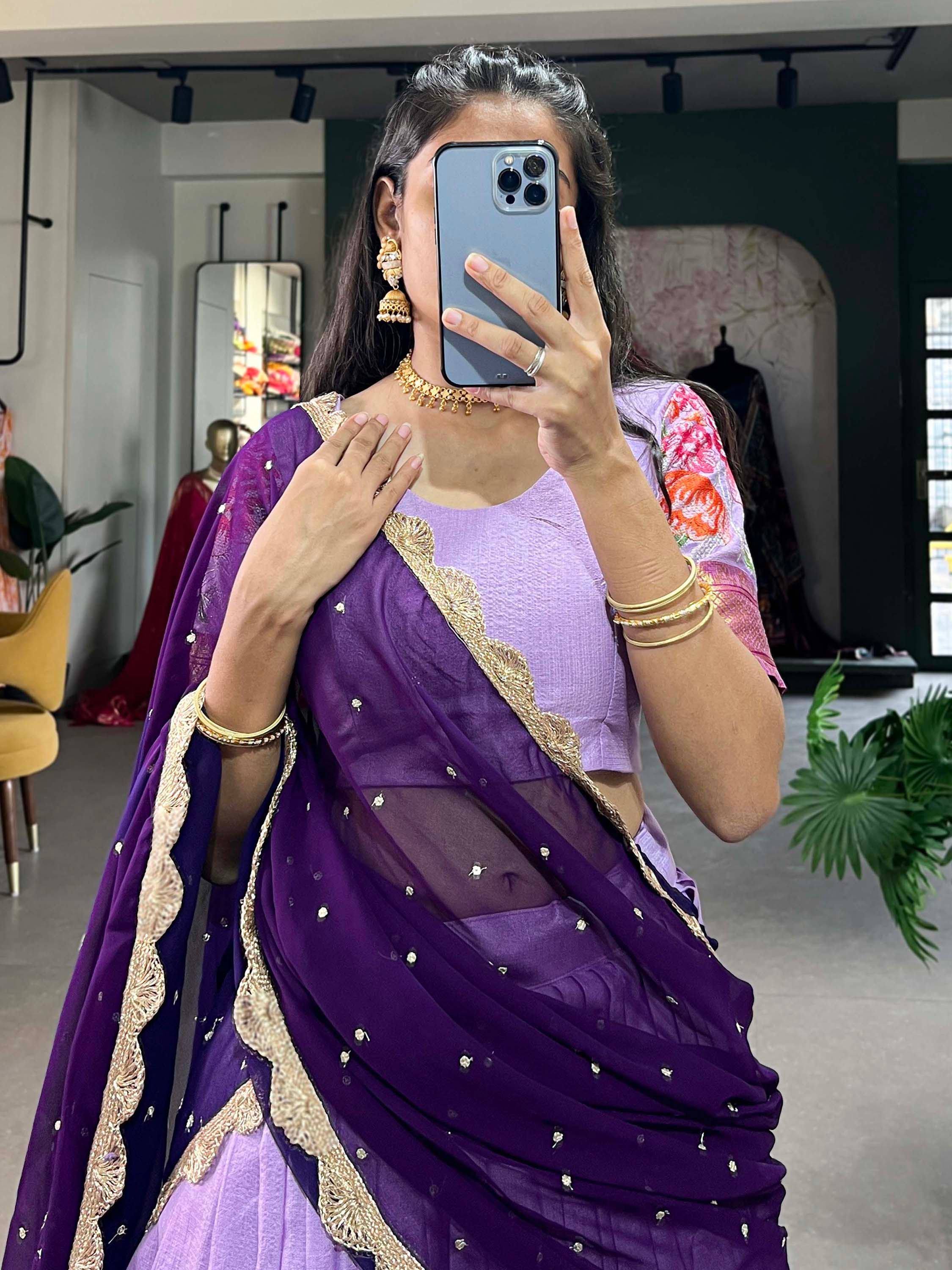 Woman in purple saree with gold embroidery and floral blouse, taking mirror selfie in boutique