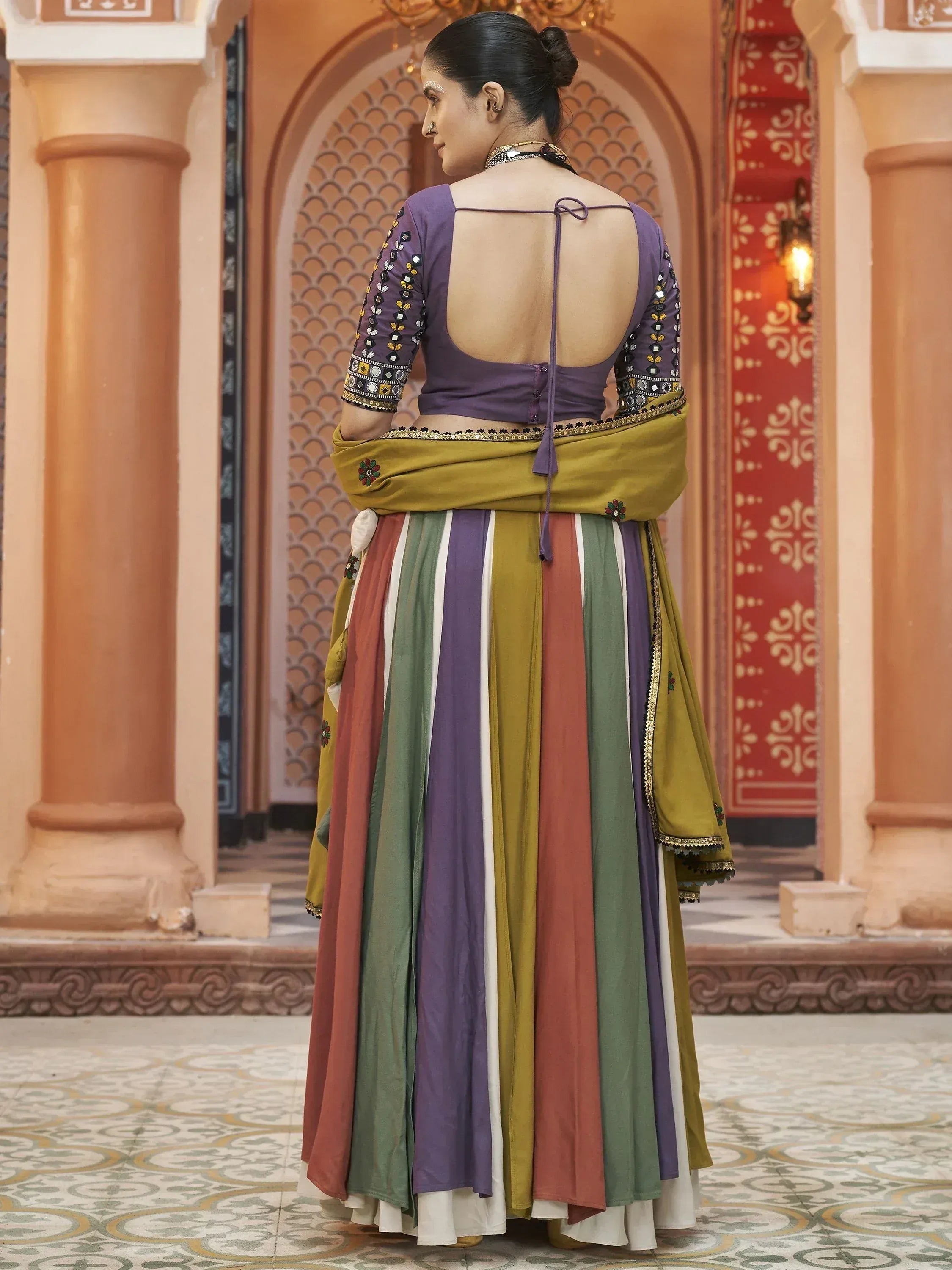 Purple backless blouse with mirror work, colorful striped lehenga, and olive dupatta for Indian ethnic wear
