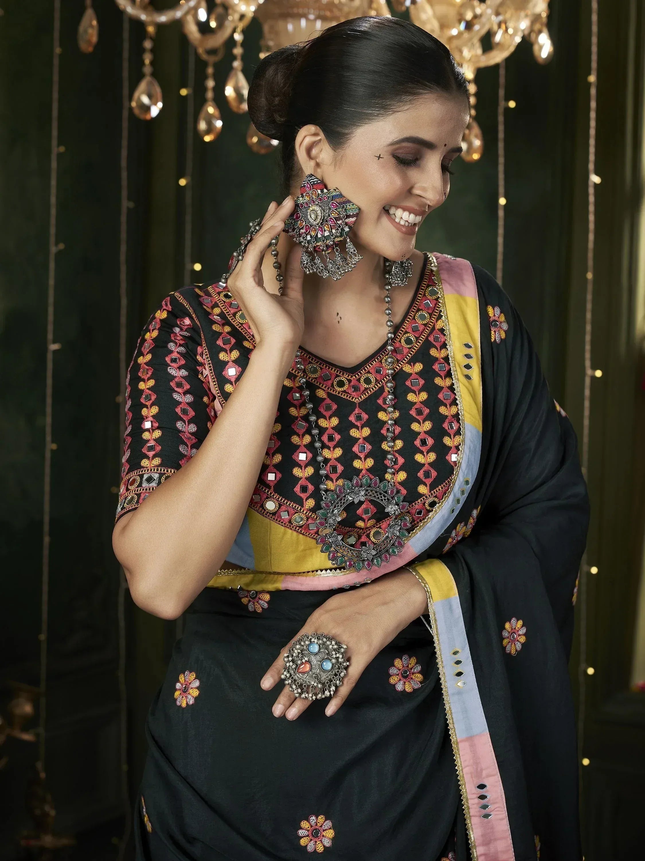Woman in black embroidered saree with mirror work, colorful blouse, and statement jewelry for Indian ethnic wear.