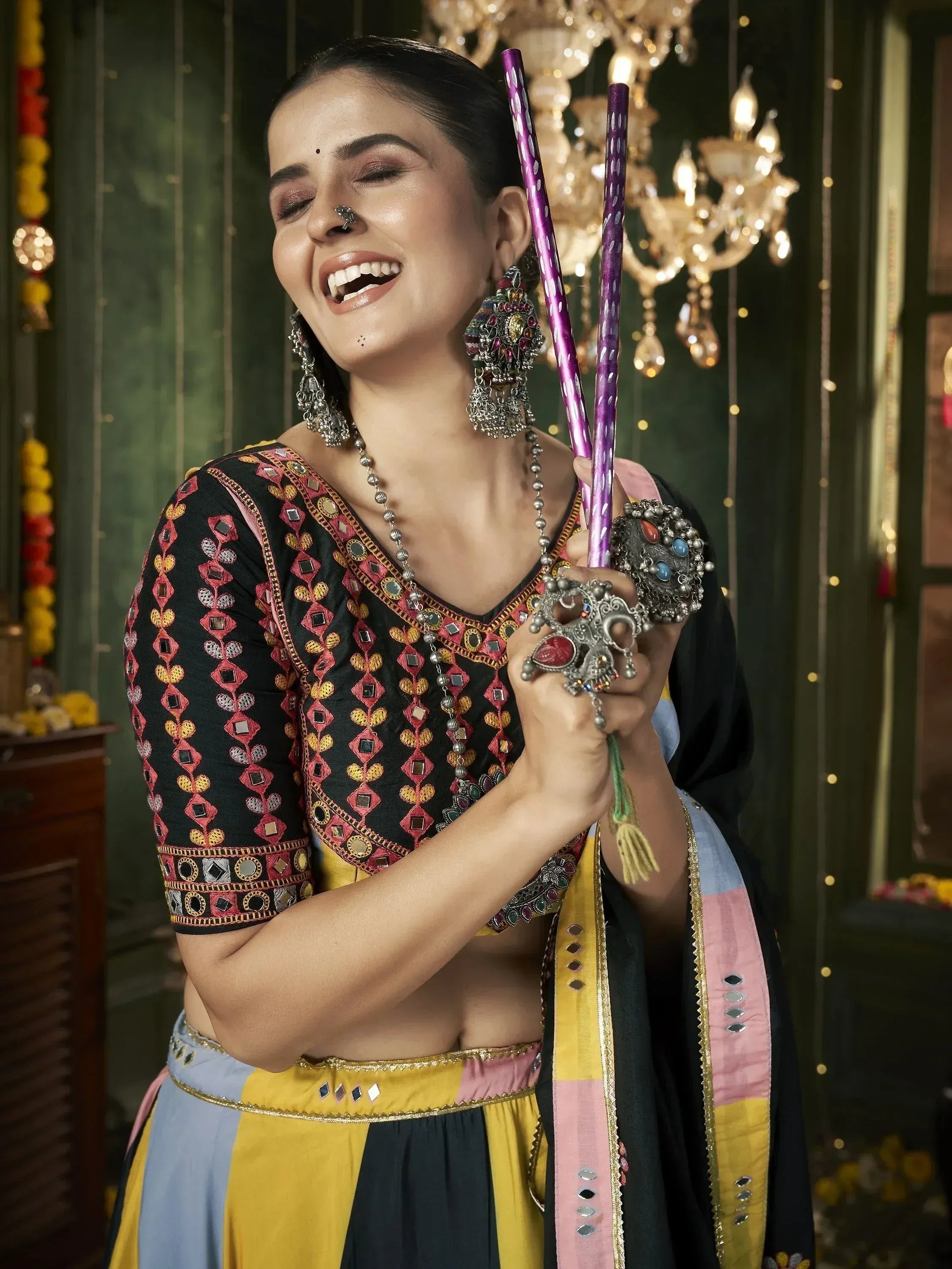 Woman in colorful ethnic wear with mirror work, holding decorative sticks, festive Indian attire