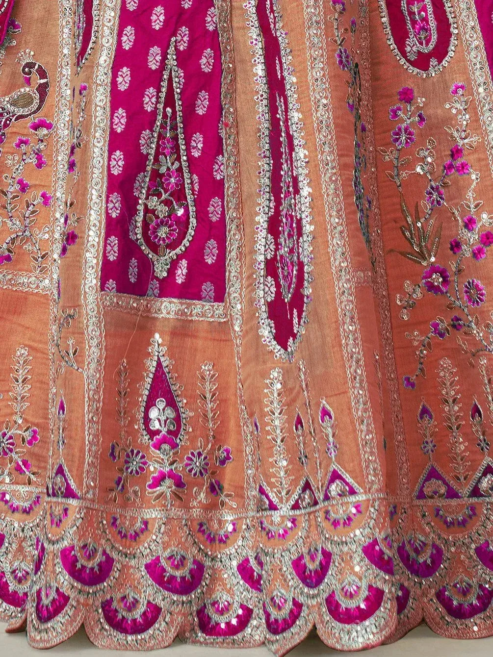 Designer lehenga with intricate floral embroidery, mirror work, and scalloped hem in peach and magenta tones