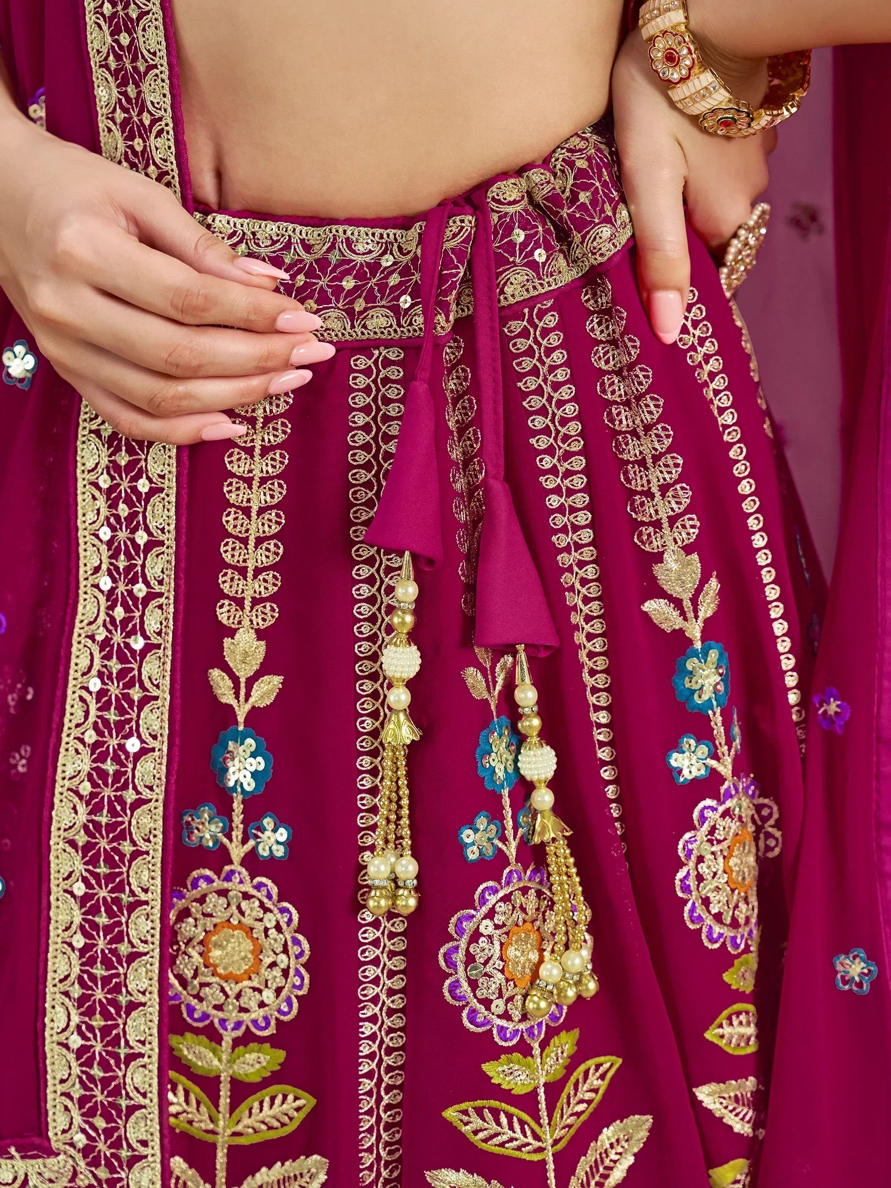 Magenta lehenga choli with gold embroidery, floral motifs, and pearl tassels for Indian ethnic wear