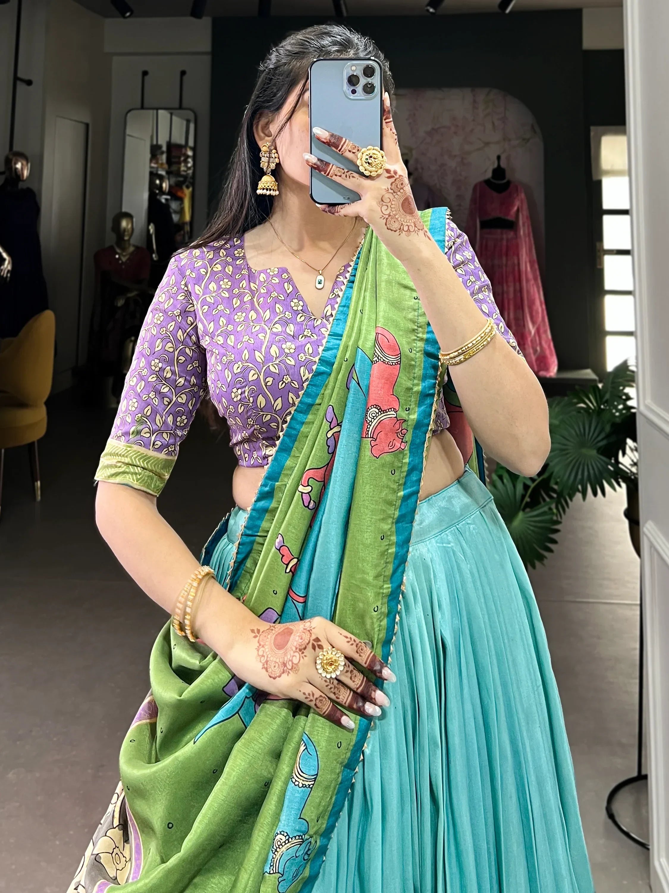 Woman in purple floral blouse, turquoise lehenga, and green printed dupatta with henna hands