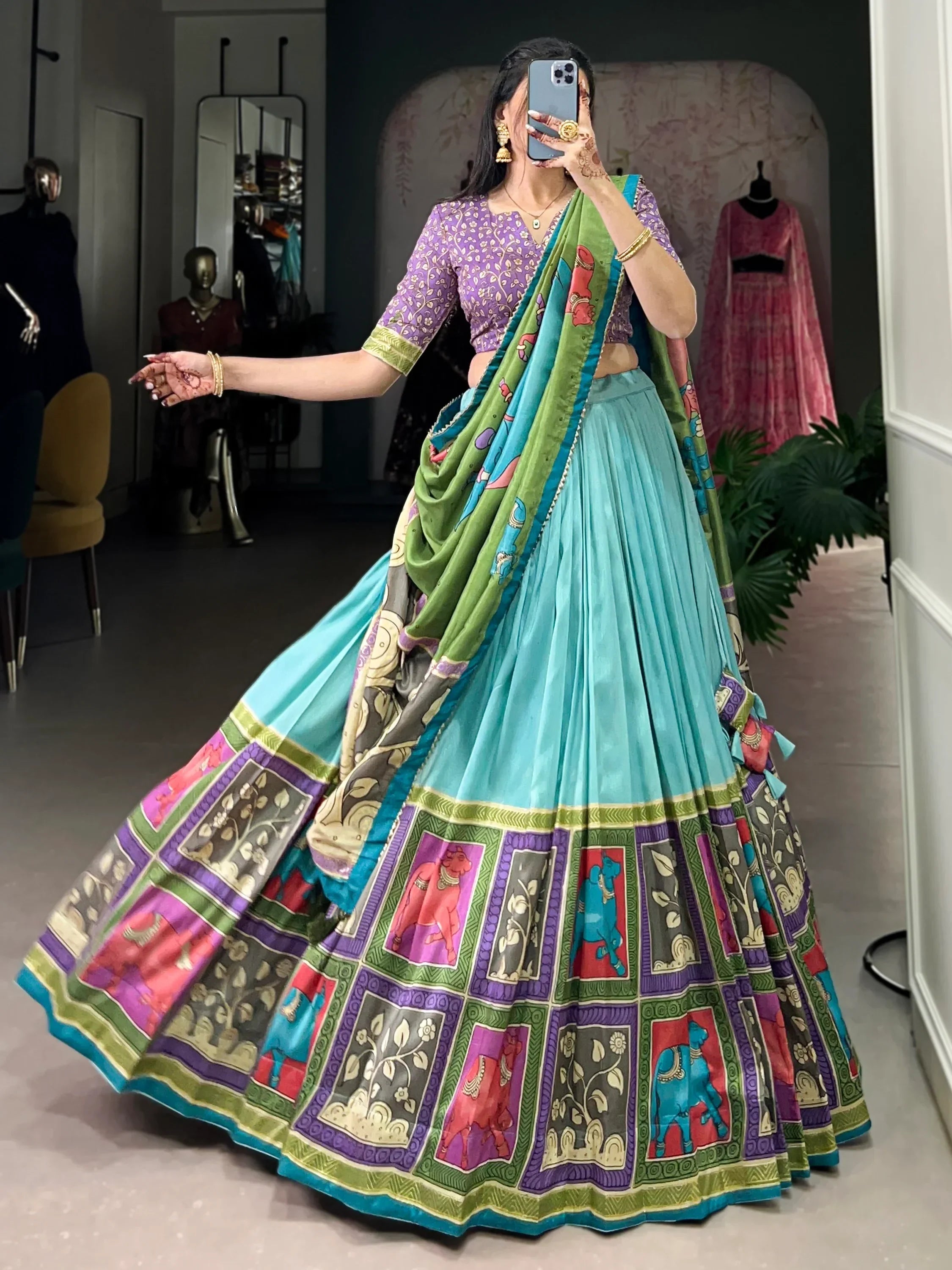 Woman in vibrant turquoise lehenga choli with elephant print, purple blouse, and green dupatta, perfect for Indian ethnic wear.
