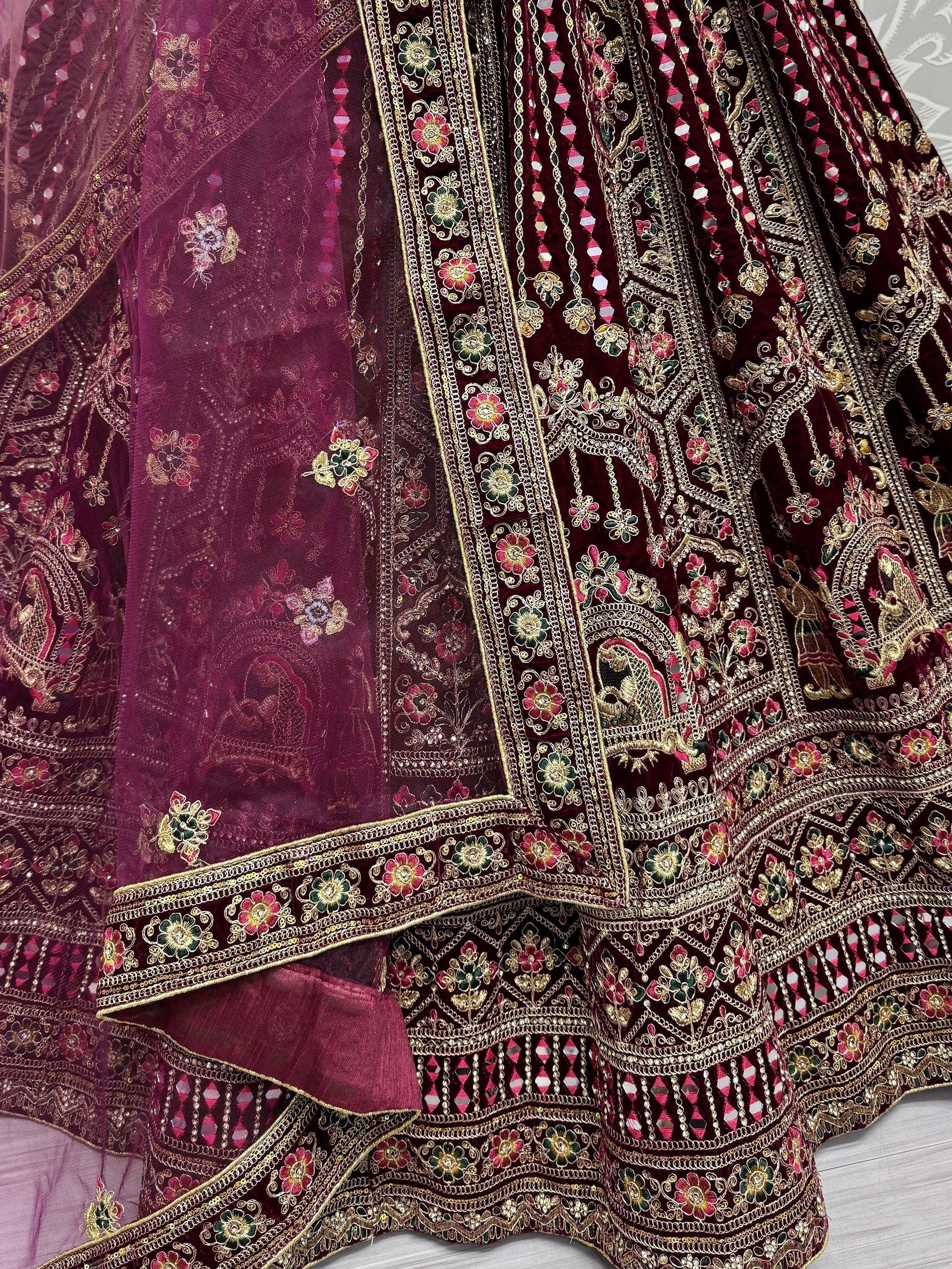 Luxury maroon velvet lehenga choli with intricate gold embroidery and mirror work, perfect for Indian weddings.