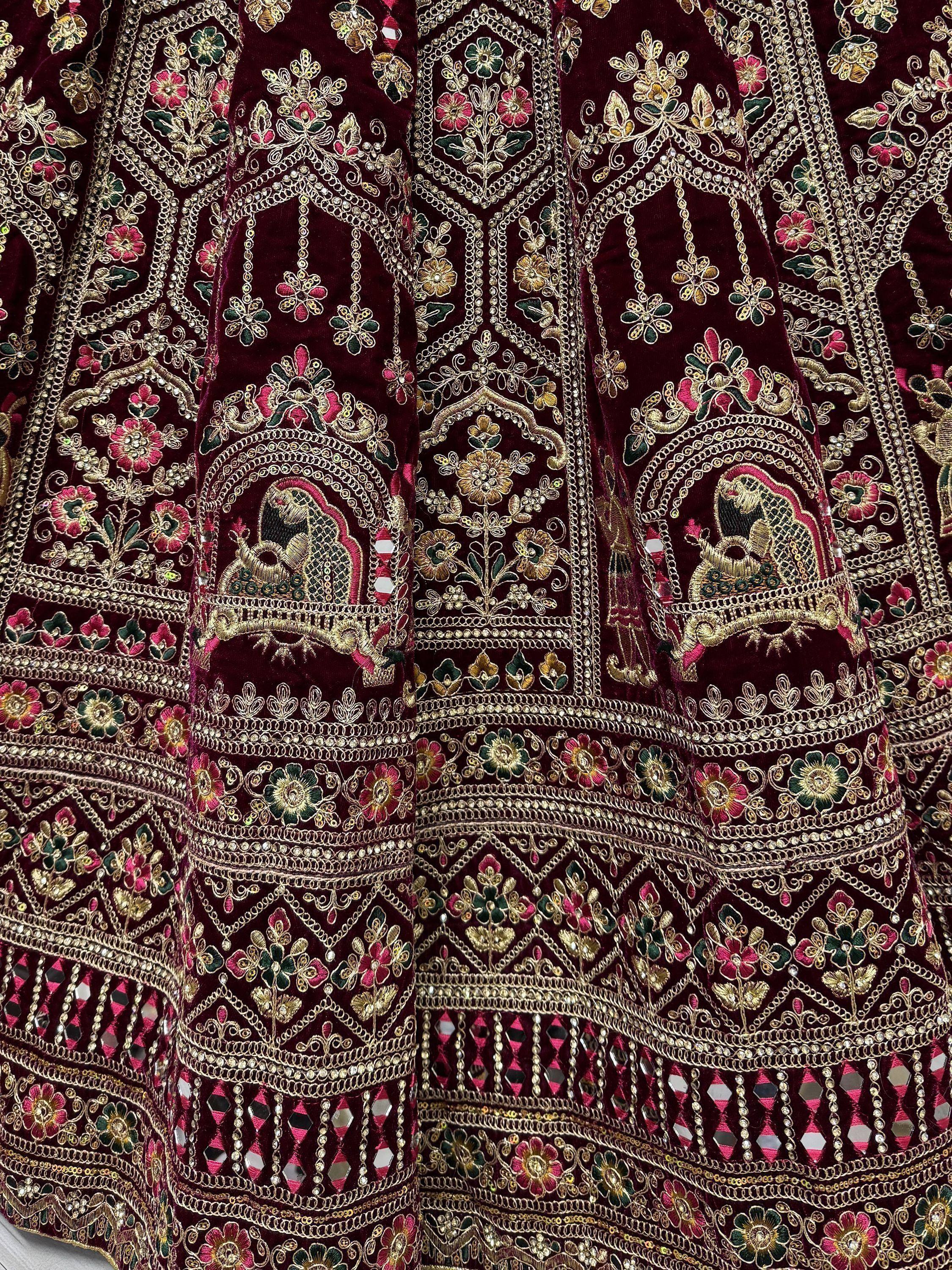 Luxury maroon velvet lehenga with intricate gold embroidery, floral motifs, and mirror work for Indian ethnic wear.