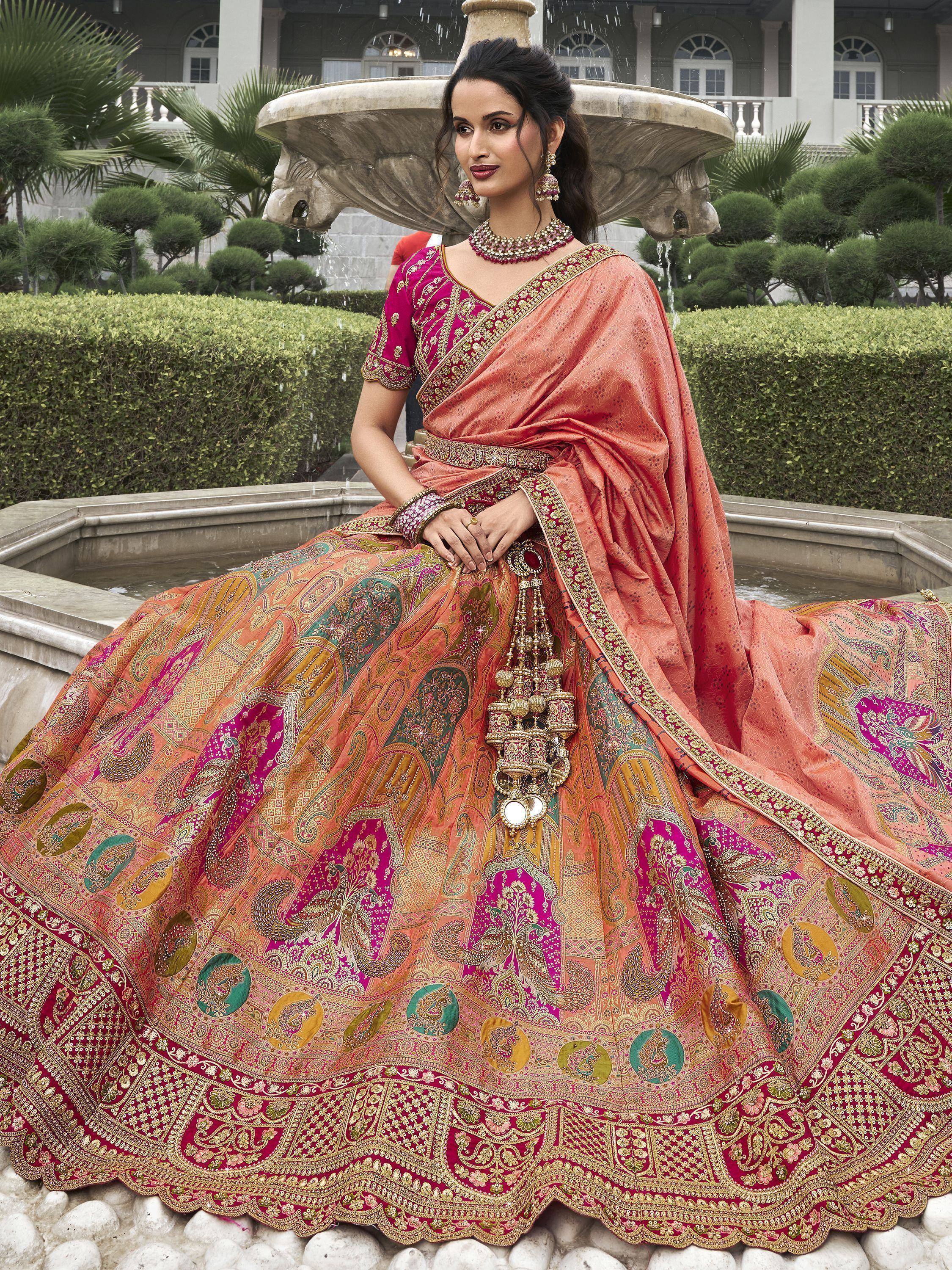 Woman in vibrant pink and peach designer lehenga choli with intricate embroidery, seated by fountain