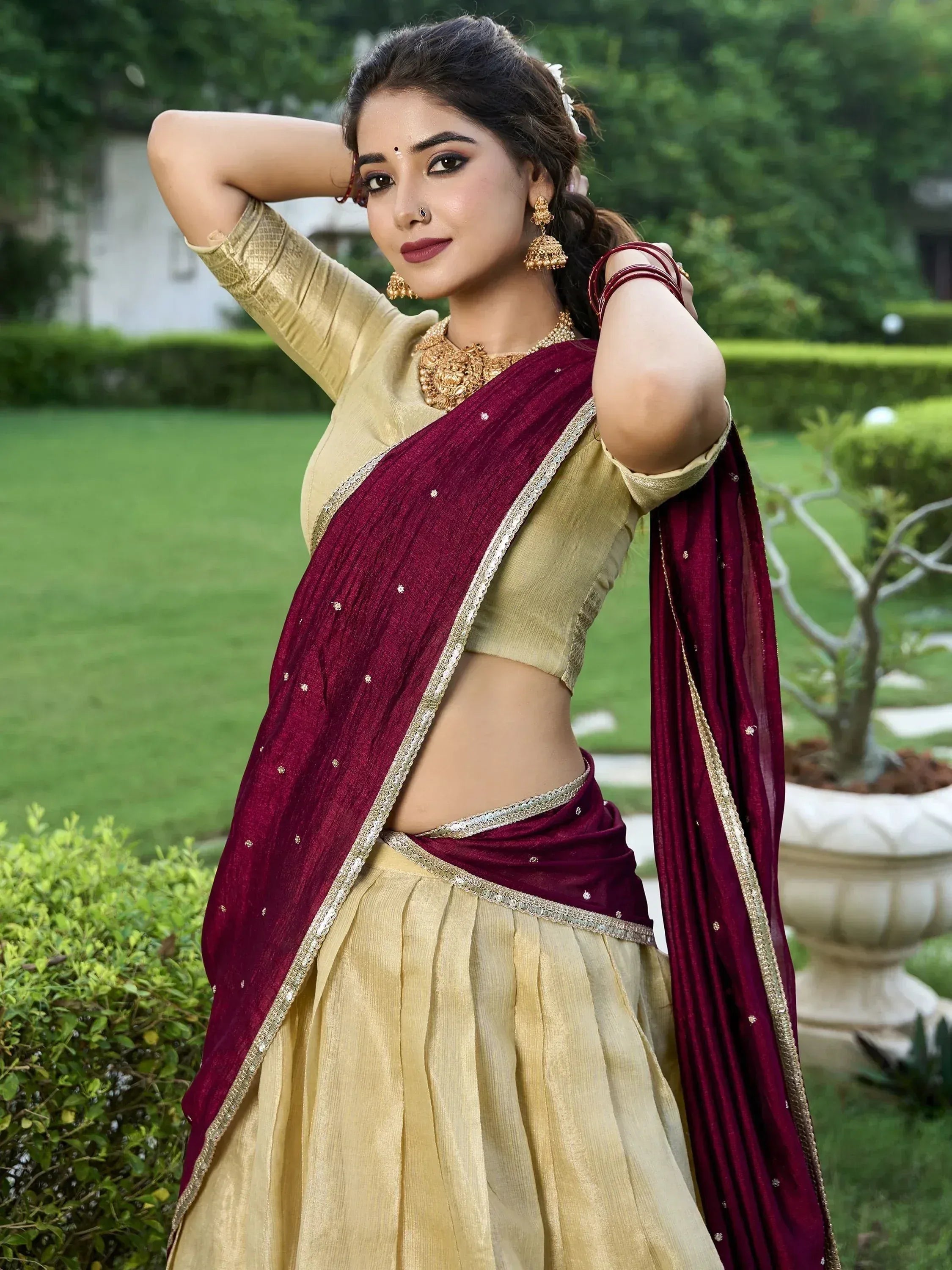 Woman in maroon and gold designer lehenga choli with ethnic jewelry, perfect for Indian weddings or festive occasions.