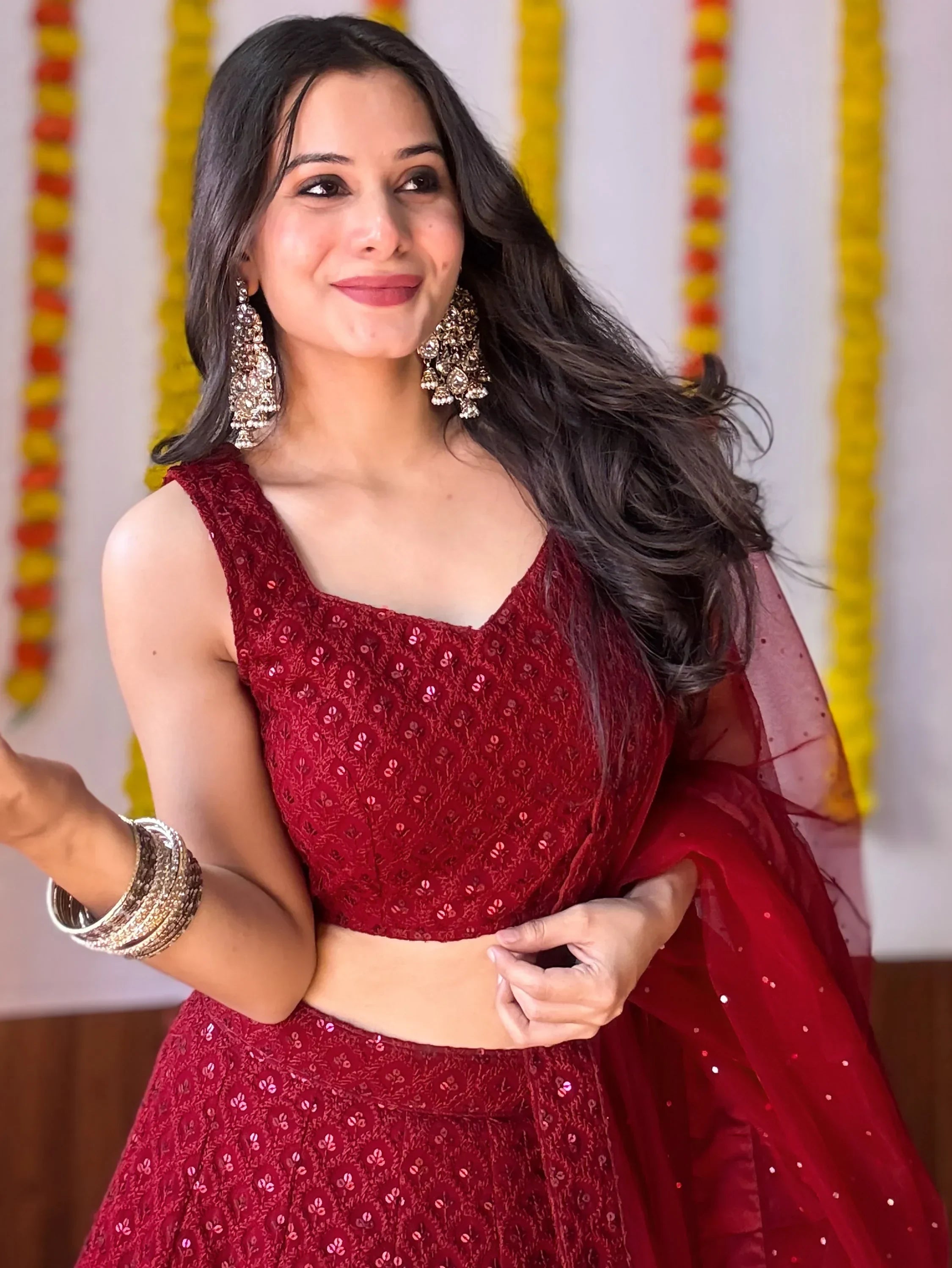 Woman in maroon sequined lehenga choli with gold earrings, festive Indian ethnic wear