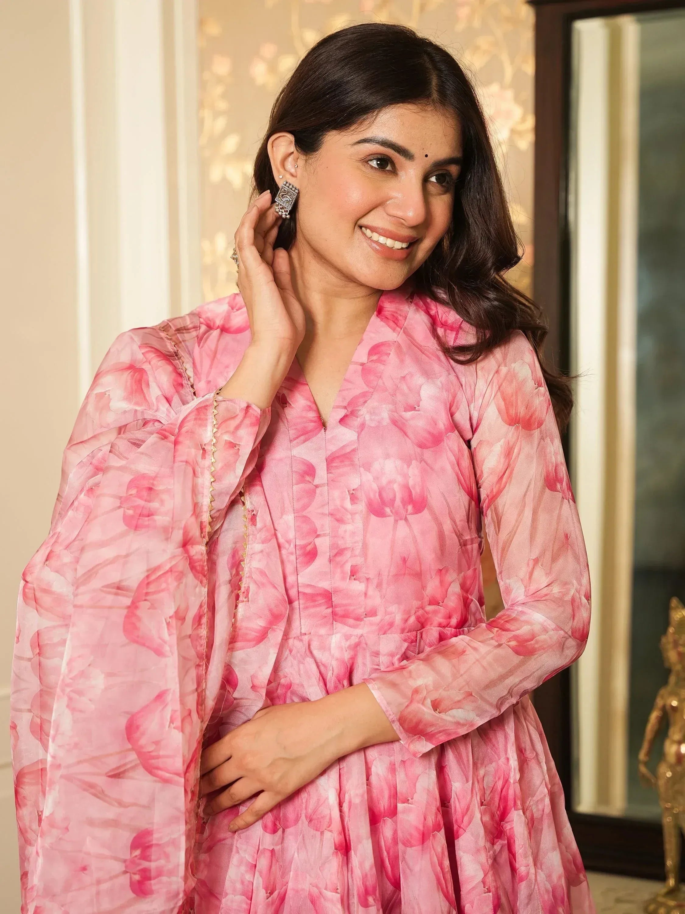 Pink floral ethnic gown with sheer sleeves and gold trim, styled with traditional earrings