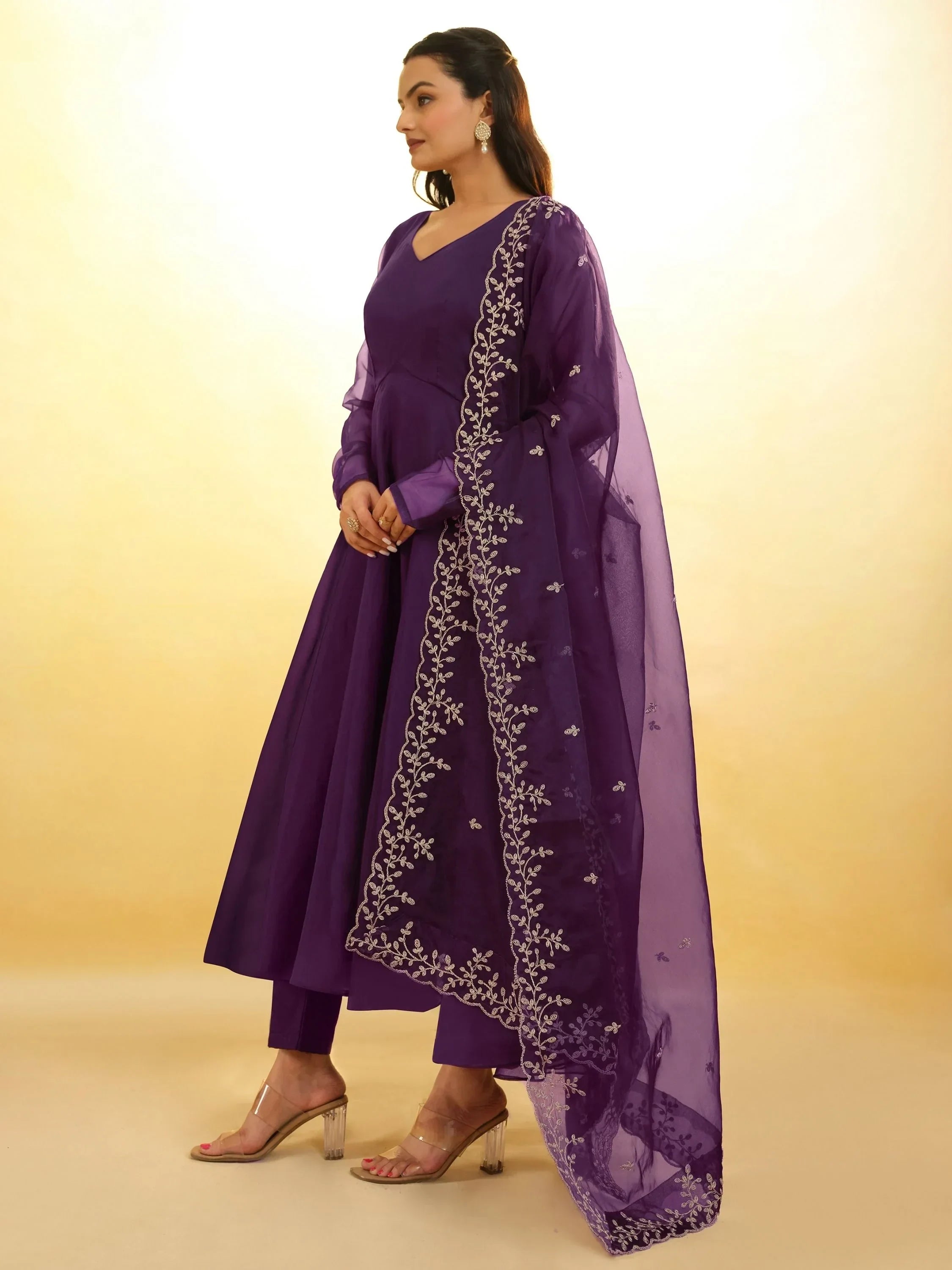 Woman in purple ethnic salwar kameez with embroidered dupatta, clear heels, and earrings