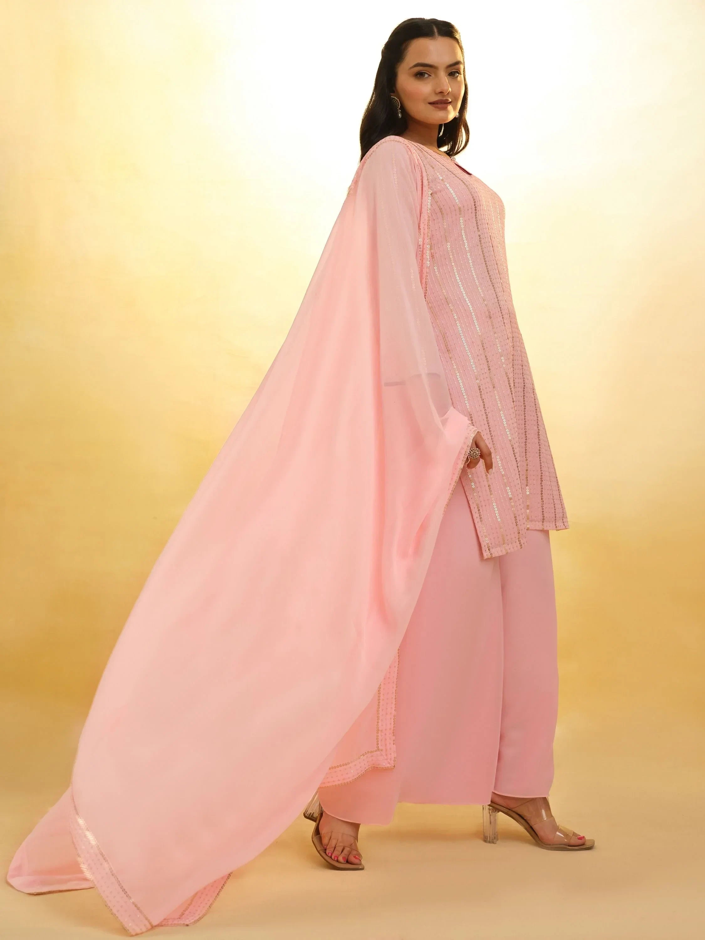 Woman in pastel pink salwar kameez with dupatta, Indian ethnic wear, standing on beige background