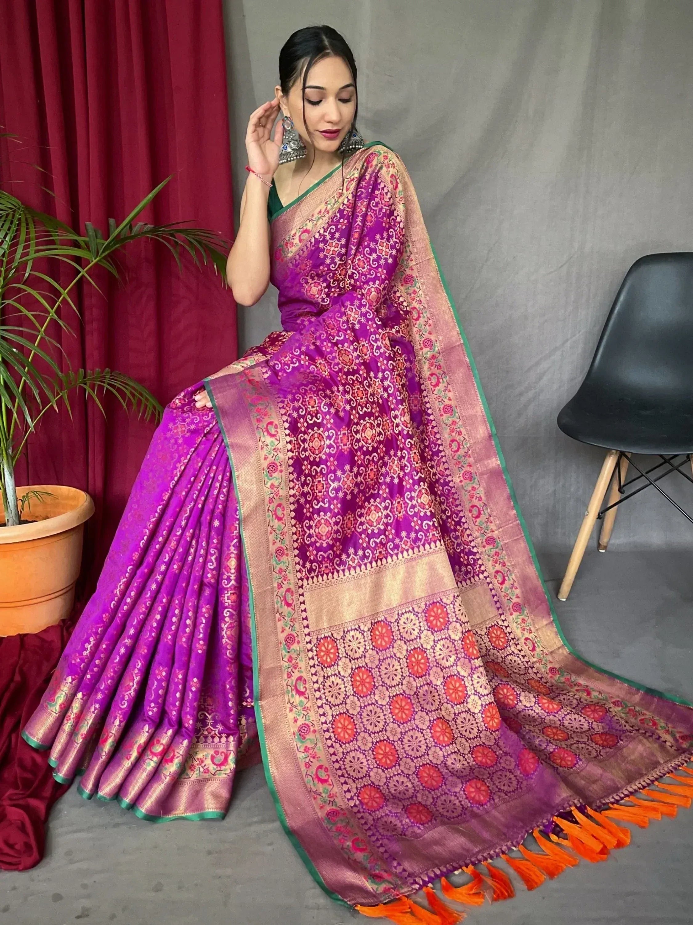 Woman in vibrant purple designer saree with intricate gold and red patterns, orange tassels, and green border.