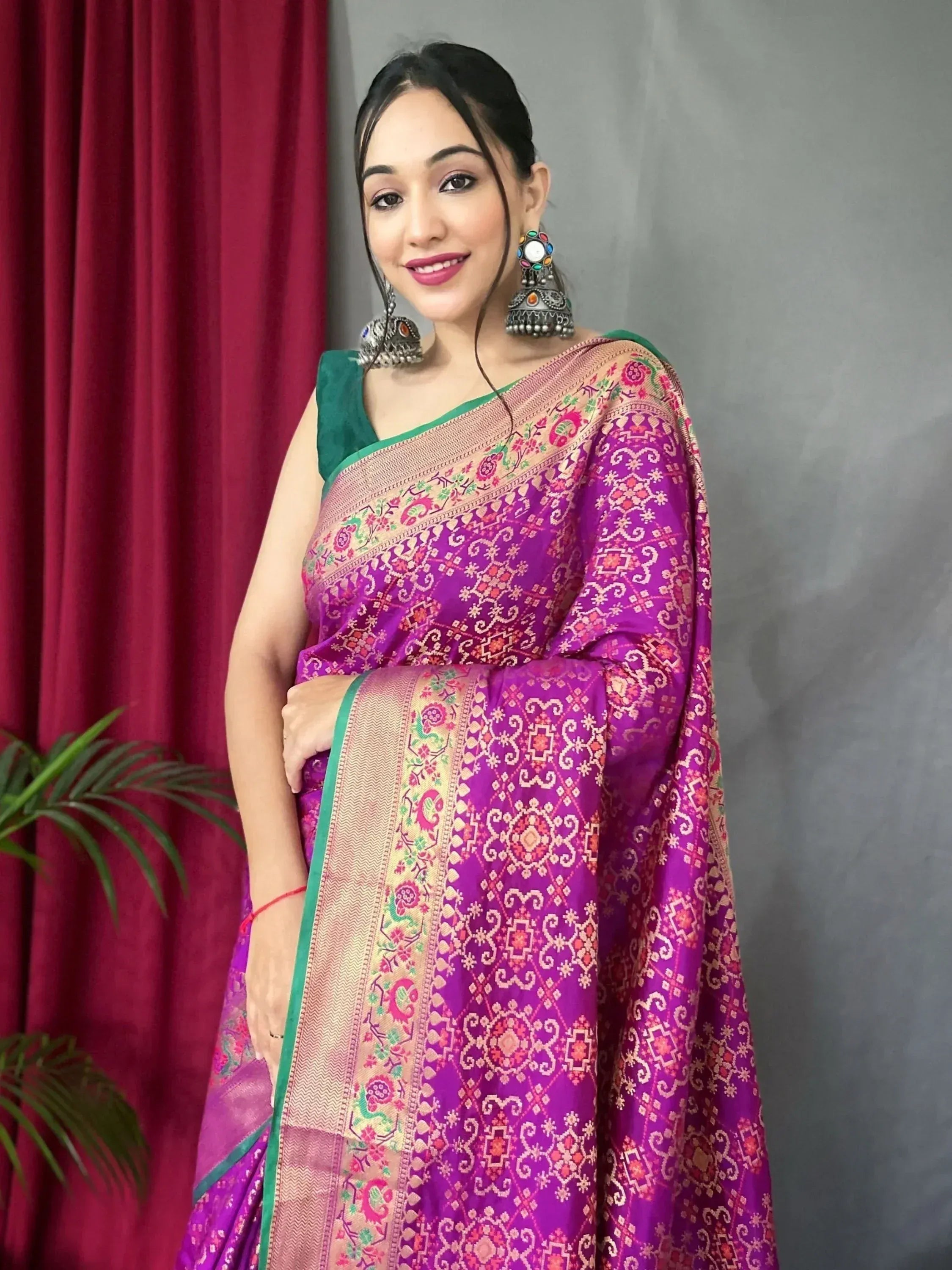 Woman in vibrant purple ethnic saree with floral gold border and green blouse, paired with statement earrings