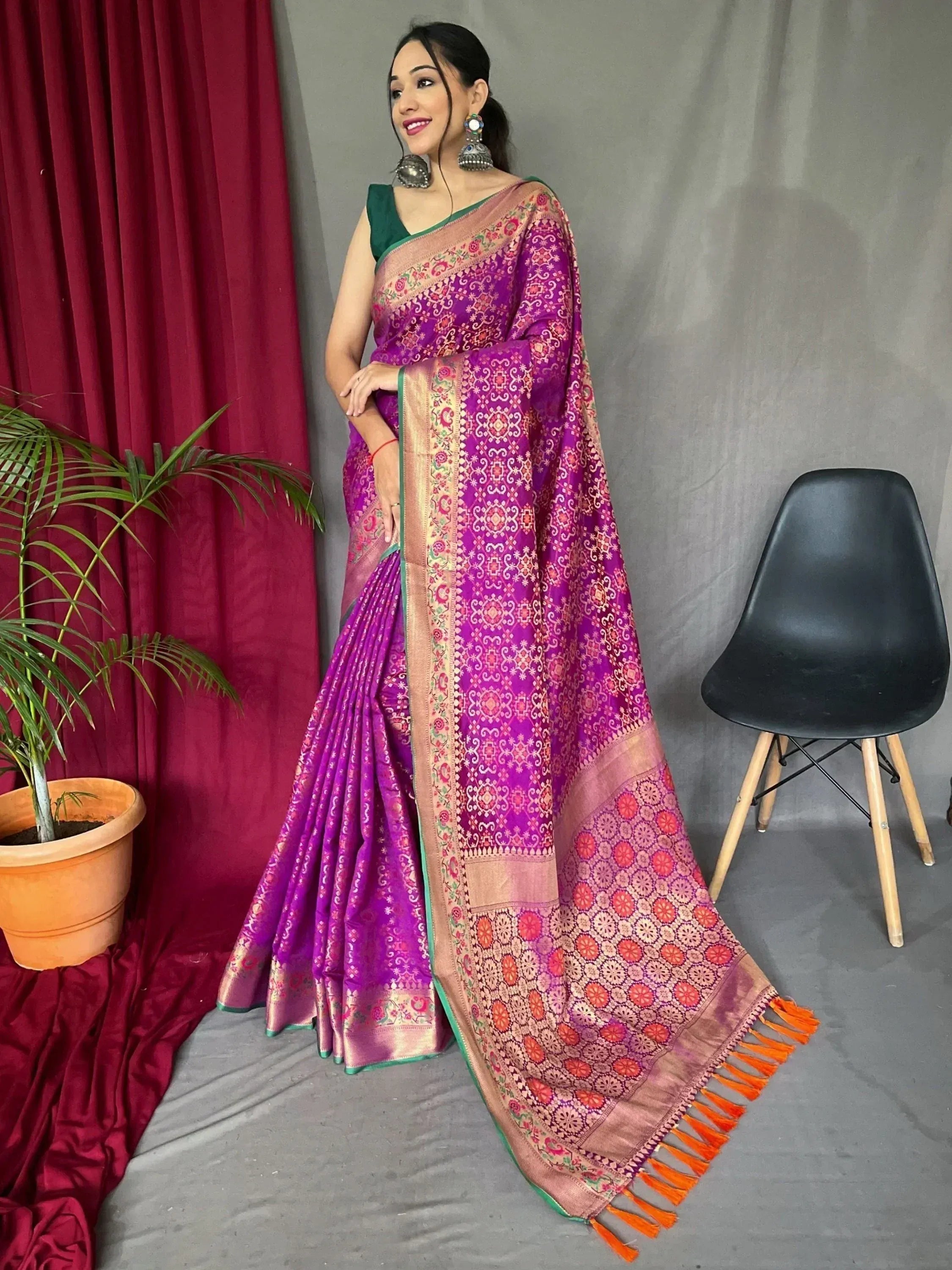 Purple designer saree with floral motifs, gold border, and orange tassels, paired with green blouse