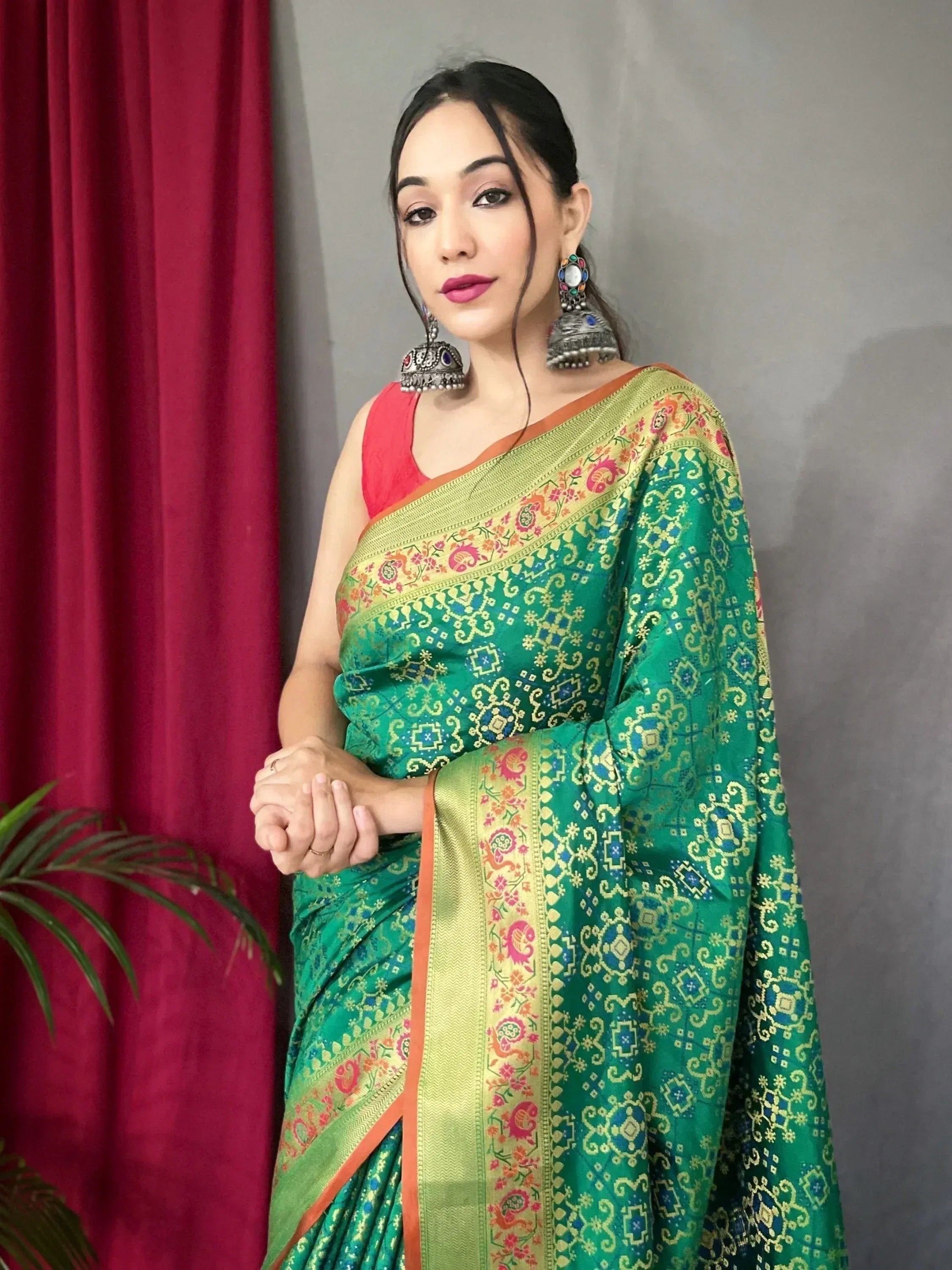 Woman in vibrant green printed saree with gold border and red blouse, styled with jhumka earrings for ethnic wear.